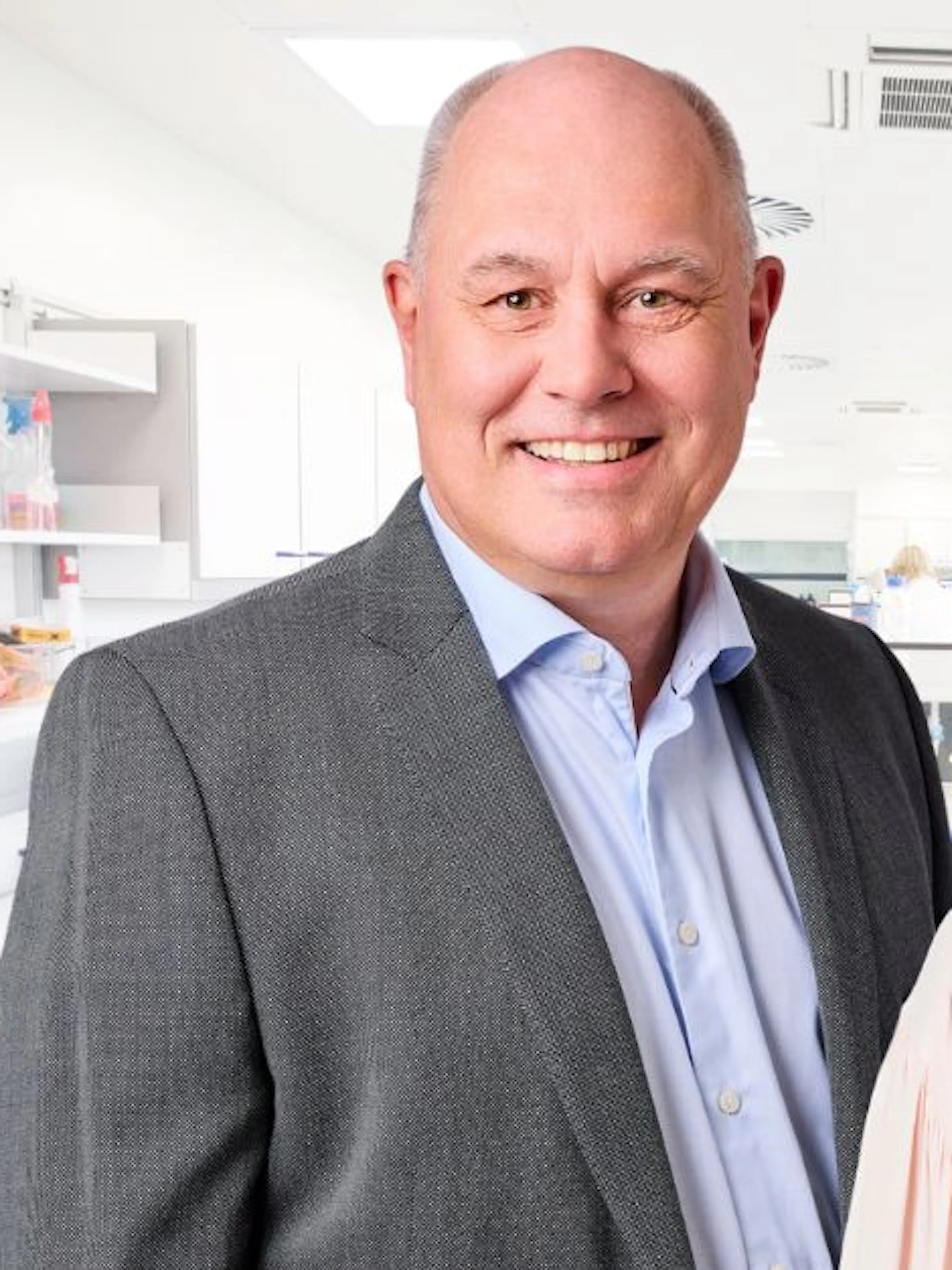 Man med ljusblå skjorta och grå kavaj, kvinna med svart hår och ljus blus. Står framför ett medicintekniskt laboratorium.