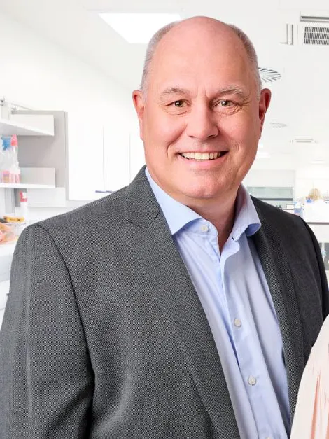 Man med ljusblå skjorta och grå kavaj, kvinna med svart hår och ljus blus. Står framför ett medicintekniskt laboratorium.