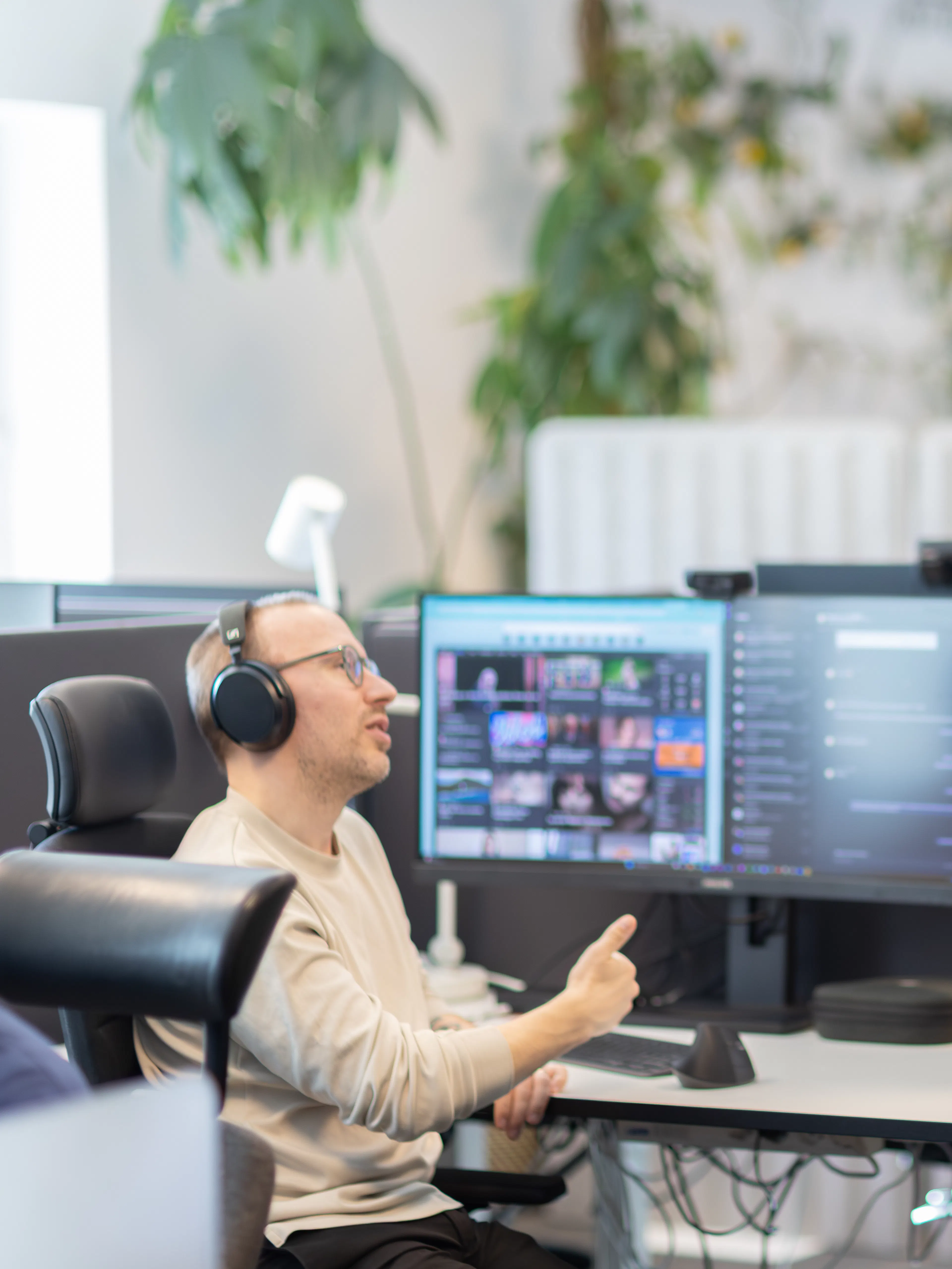 En man sitter framför ett skrivbord med tre dataskärmar, pratar med en man klädd i svart skjorta som står upp.