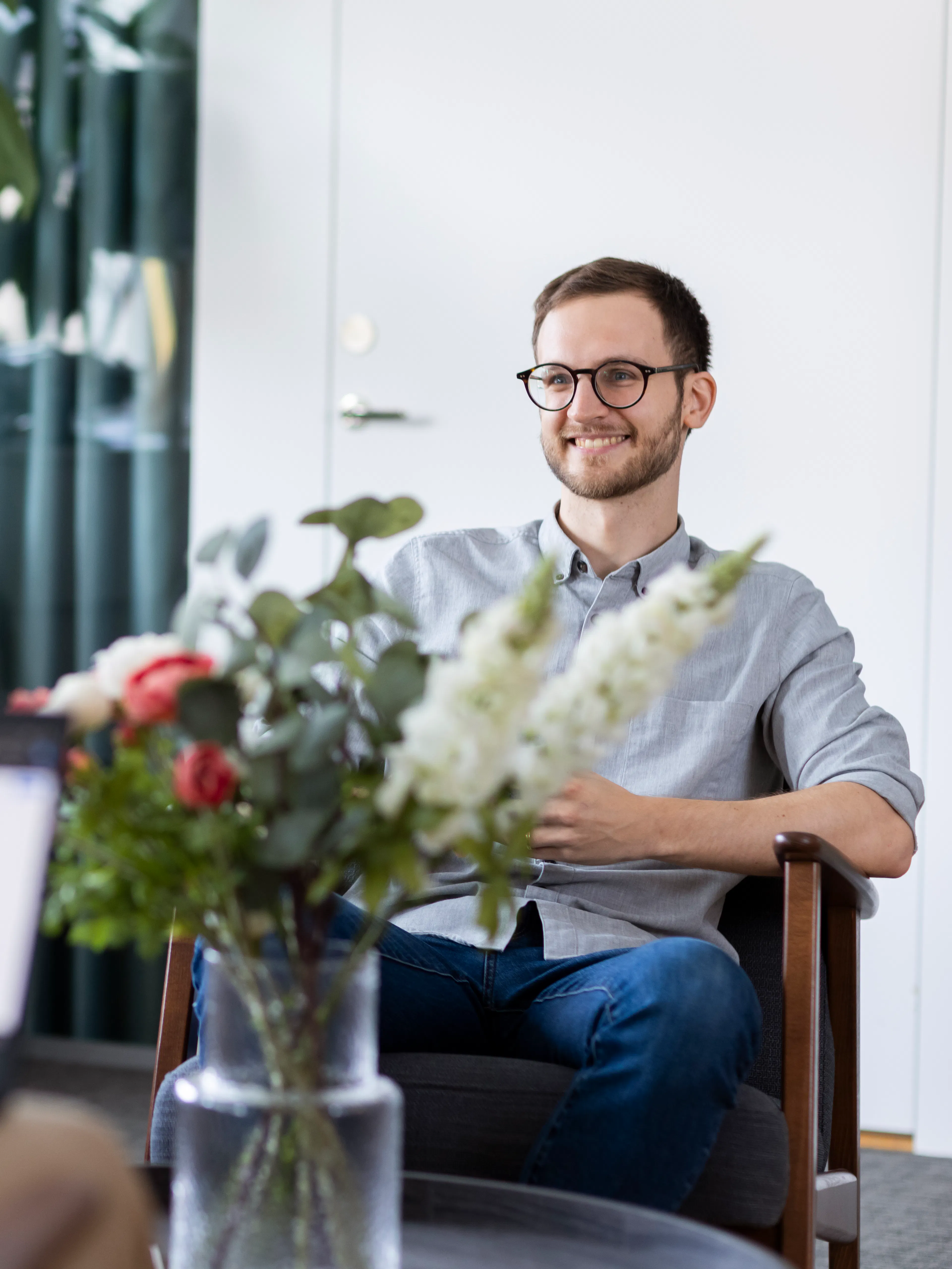 Man i ljus skjorta som sitter i en fotölj bakom en stor blomsterbukett.