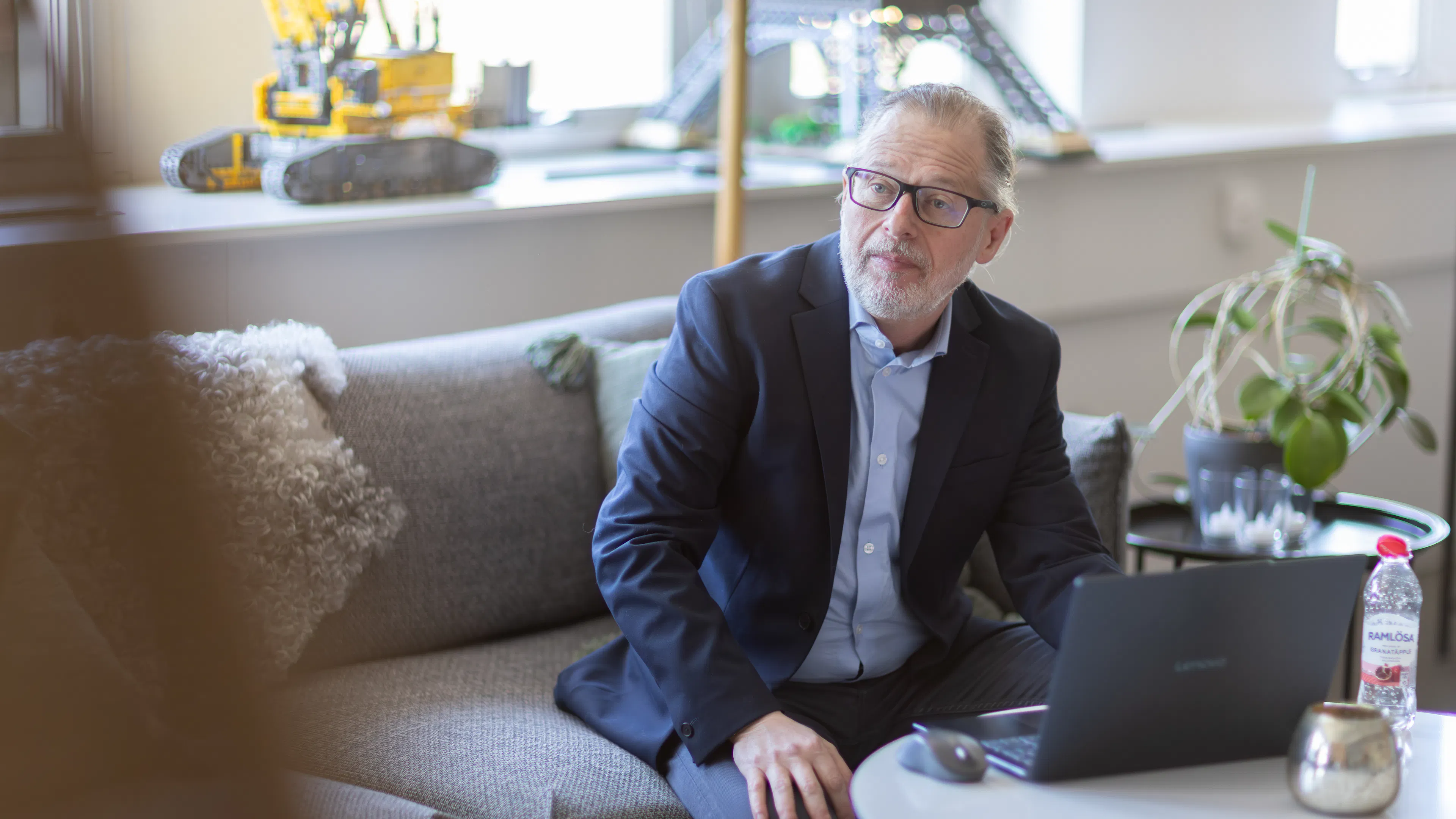 Man som sitter i blå kavaj i en soffa med en laptop på bordet