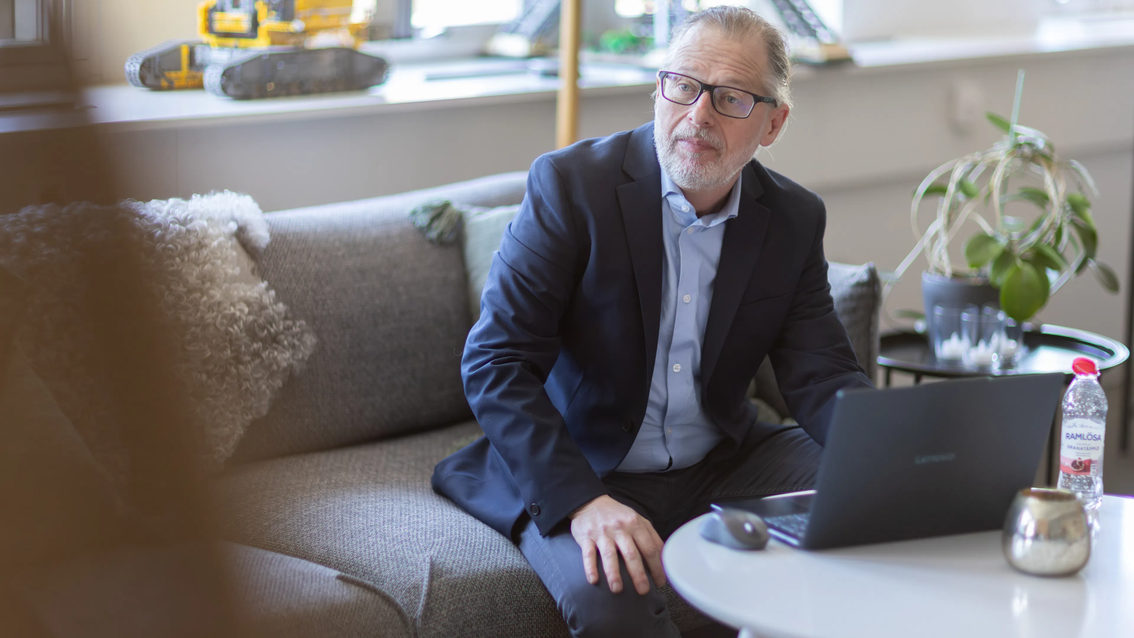 Man som sitter i blå kavaj i en soffa med en laptop på bordet