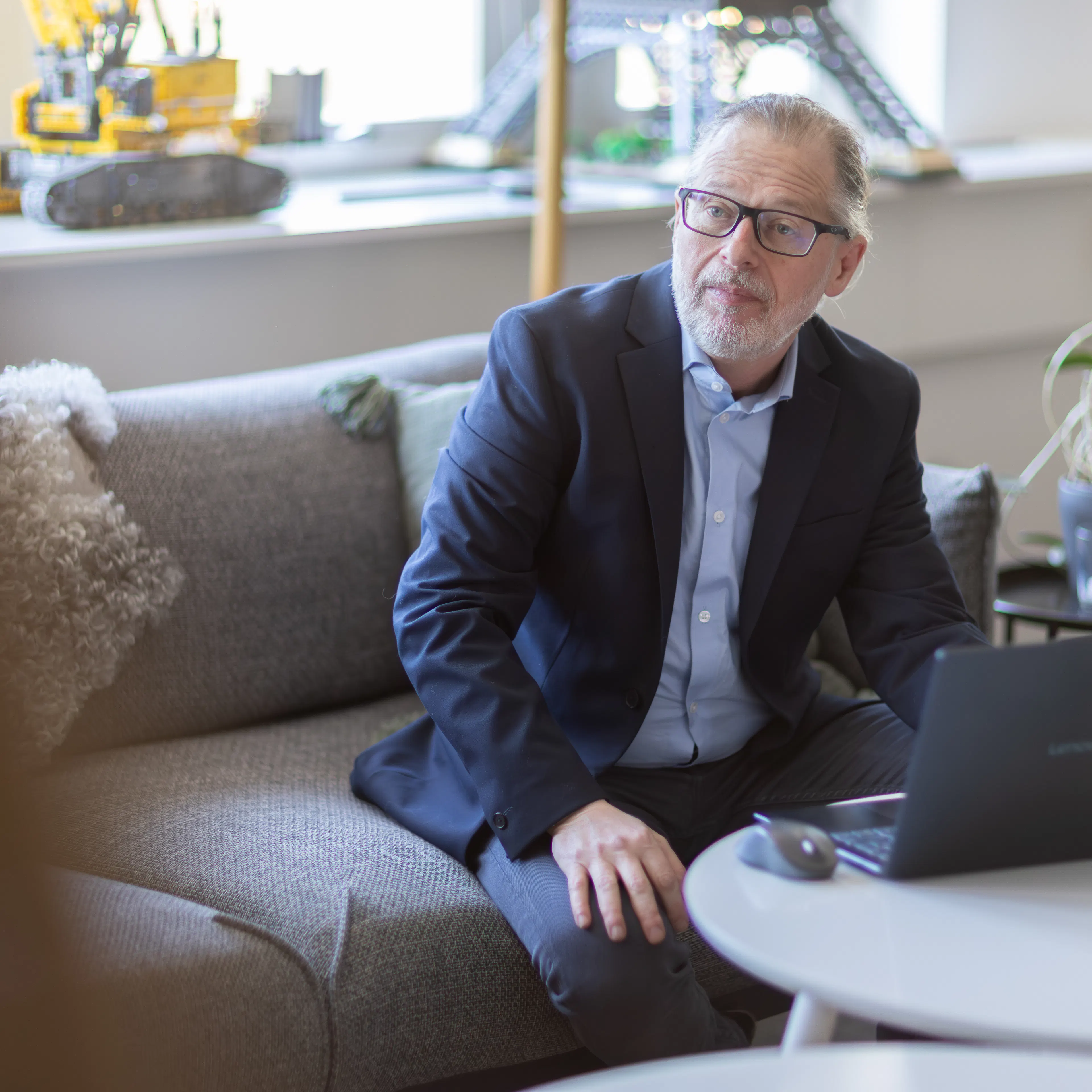 Man som sitter i blå kavaj i en soffa med en laptop på bordet