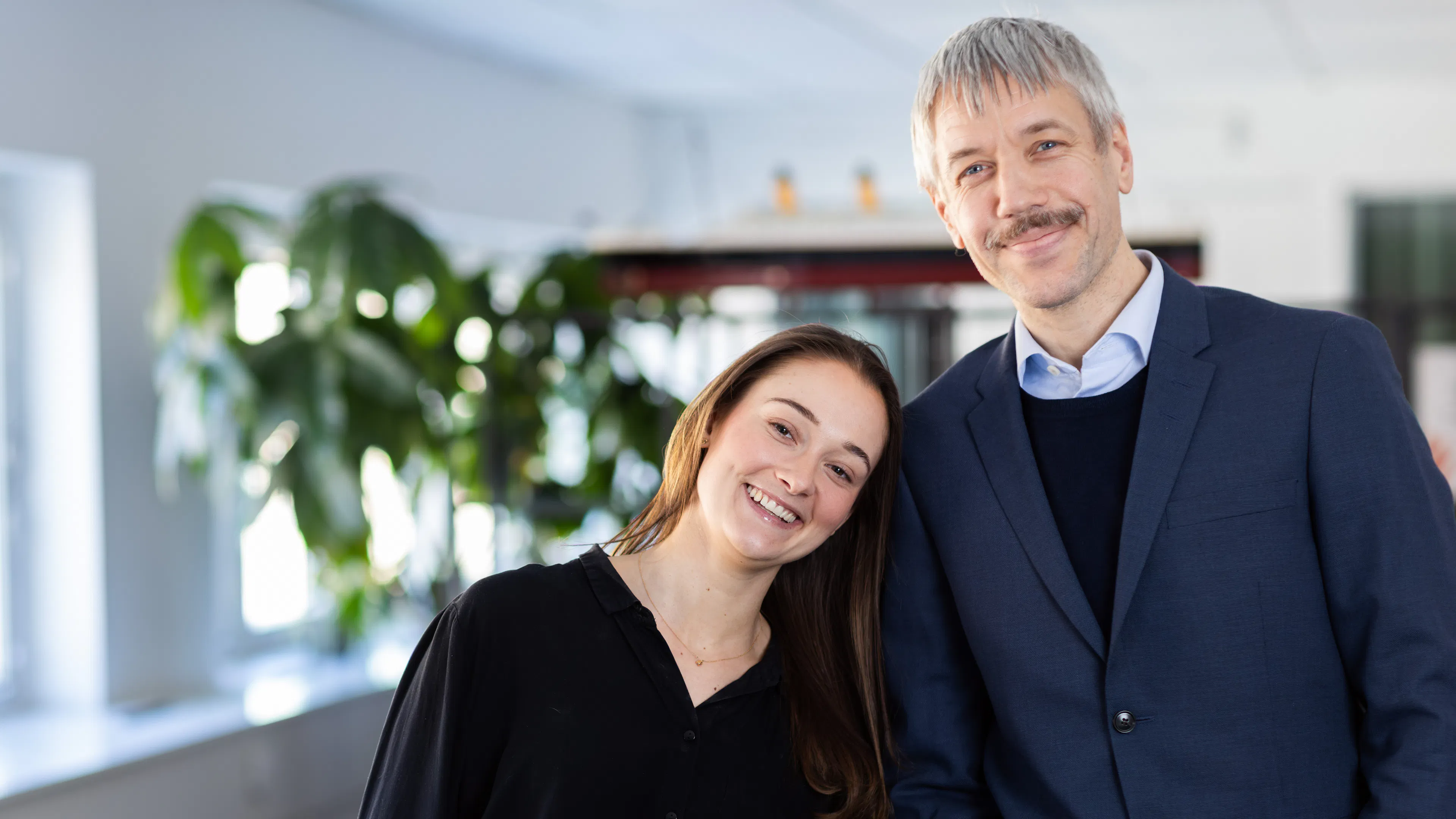 Kvinna i svart skjorta lutar sig mot en man med mustasch i blå kavaj.
