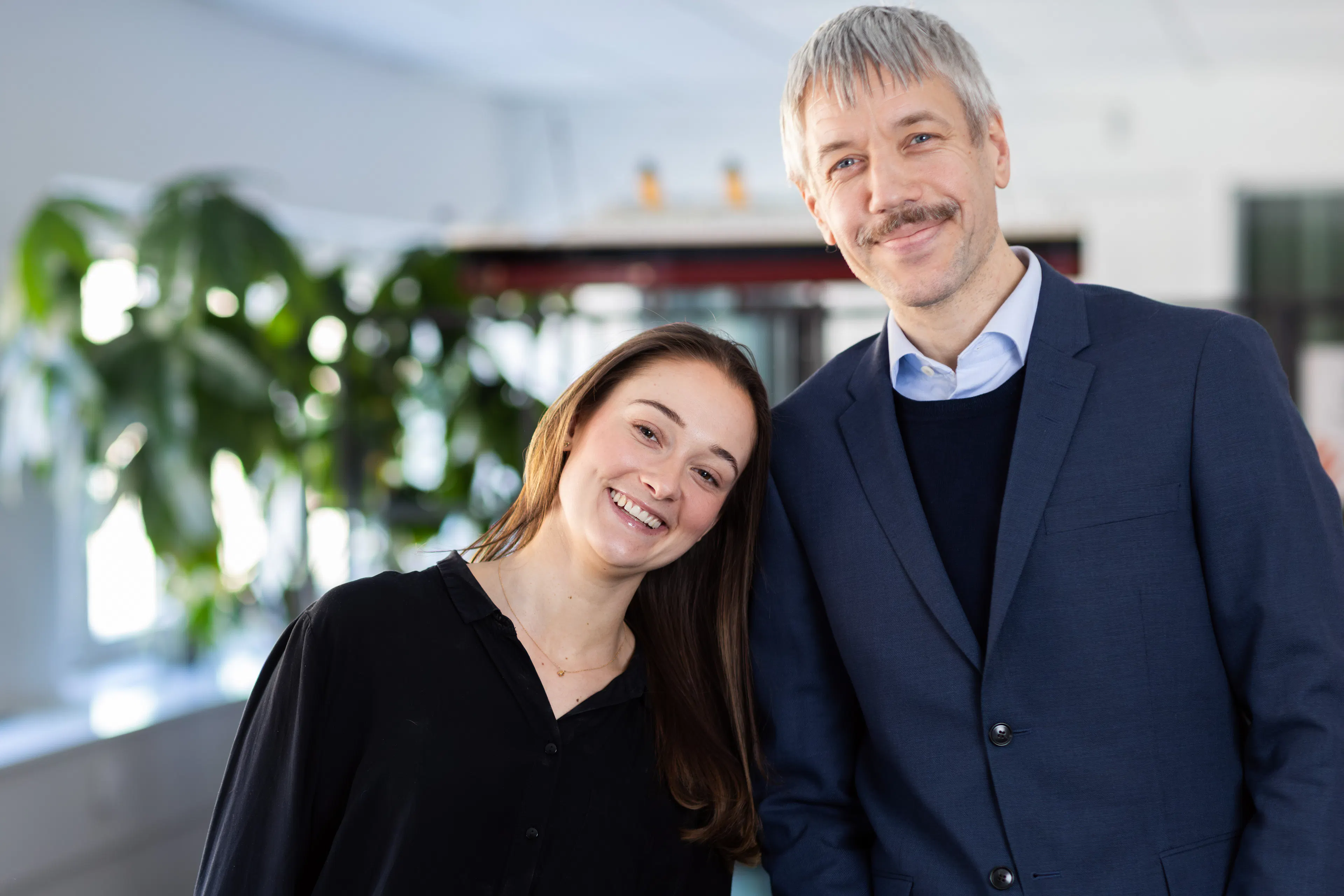 Kvinna i svart skjorta lutar sig mot en man med mustasch i blå kavaj,