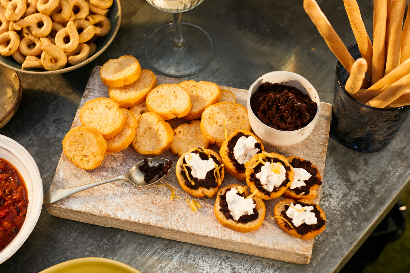 Chilli crostini are on a board, some are topped with a brown dip and white cheese, some aren't topped.