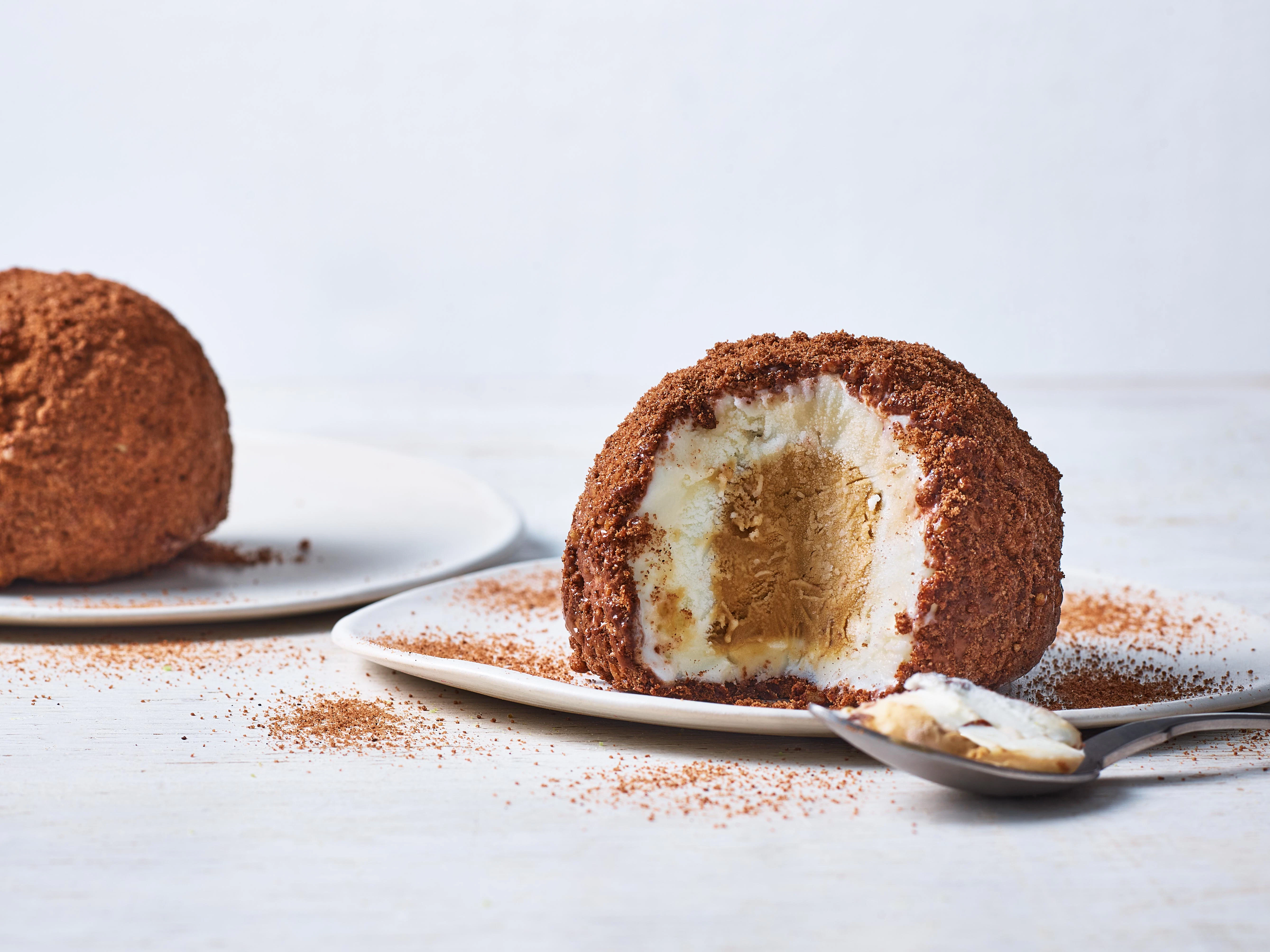 Two caffe latte tartufi, one has a quarter cut from it exposing the rings of gelato. A spoon of gelato sits on the side.