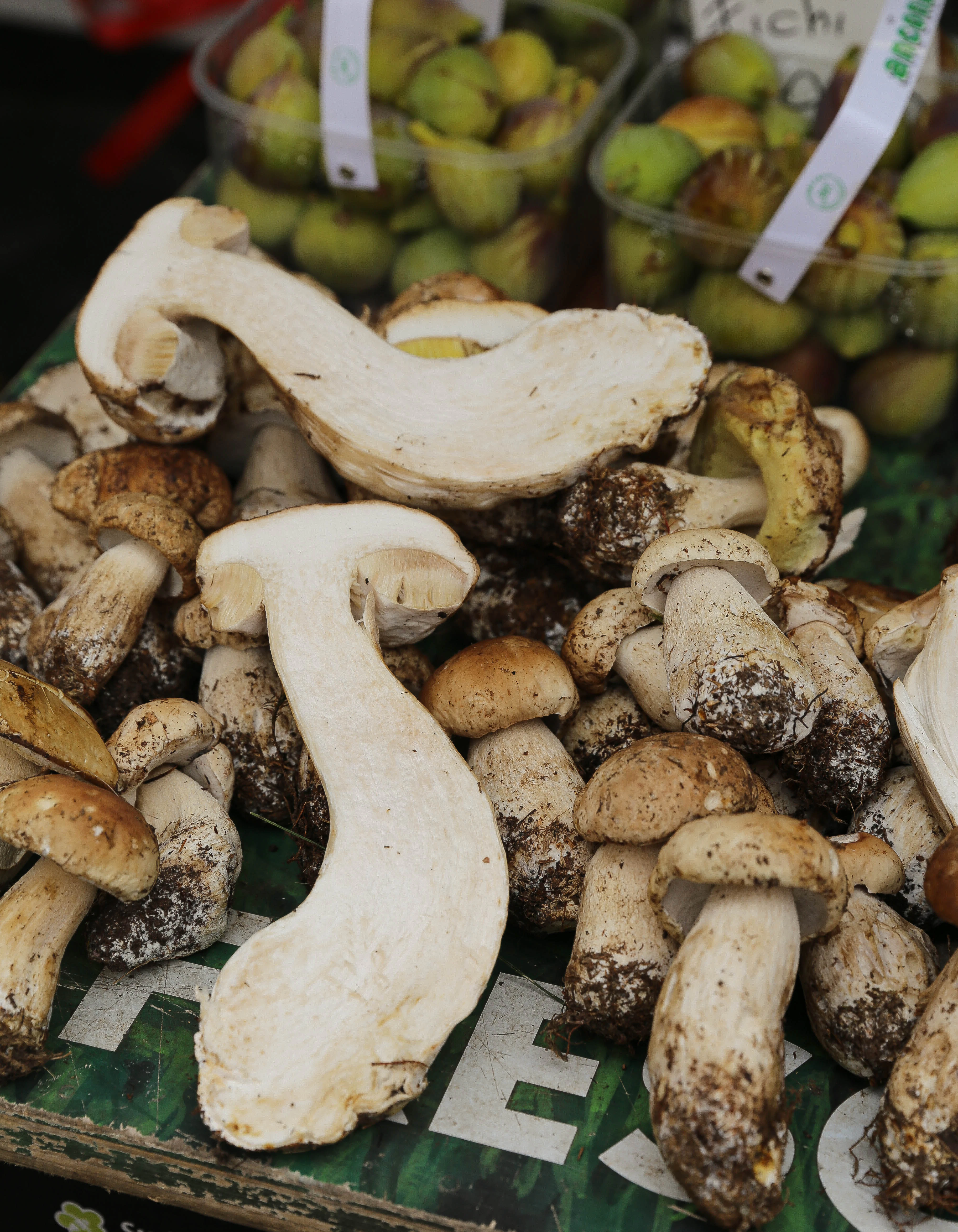 A large mushrooms has been sliced in half and placed on top of a crate of smaller mushrooms.