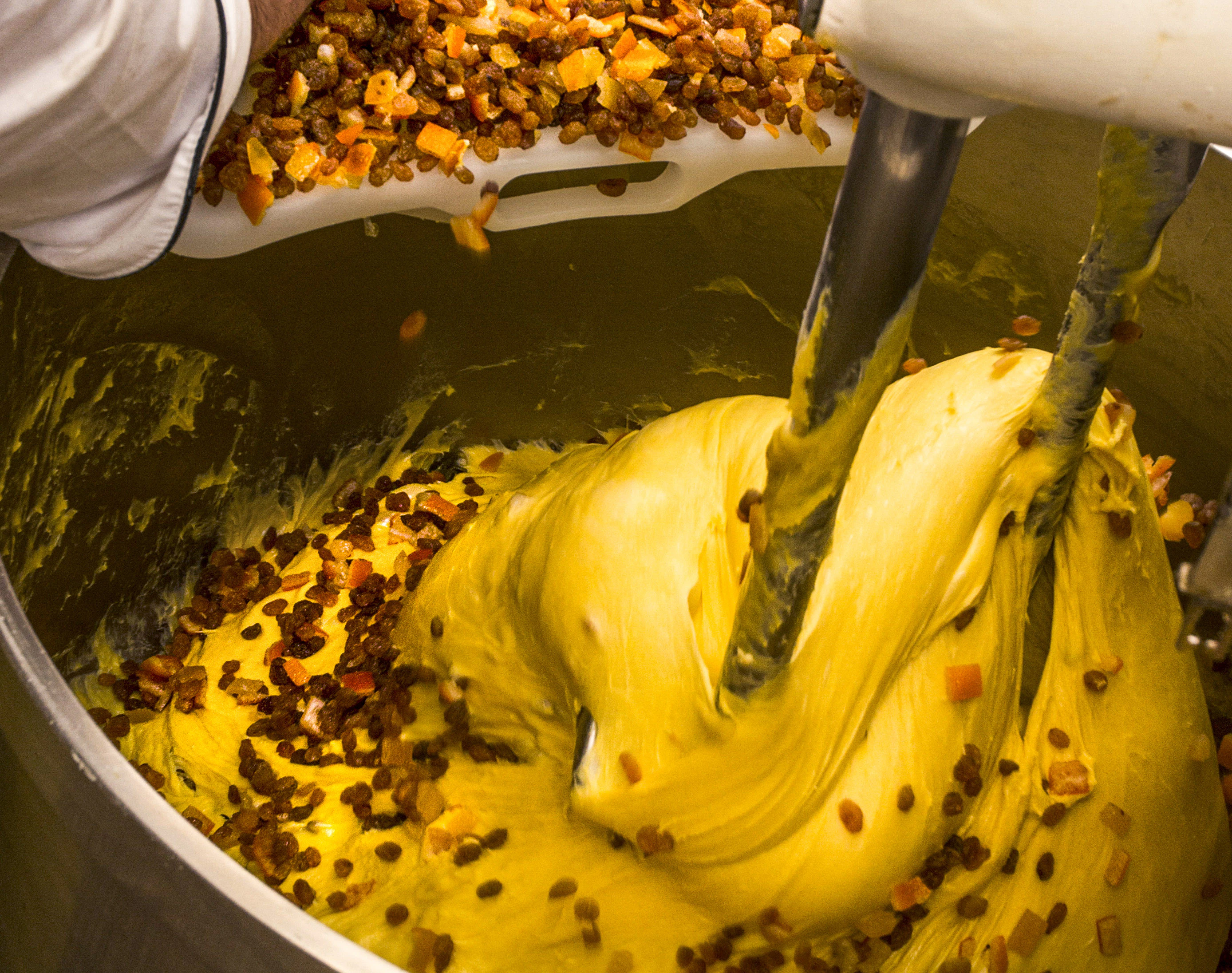 Dried fruit is added to a mixer with panettone dough in it.