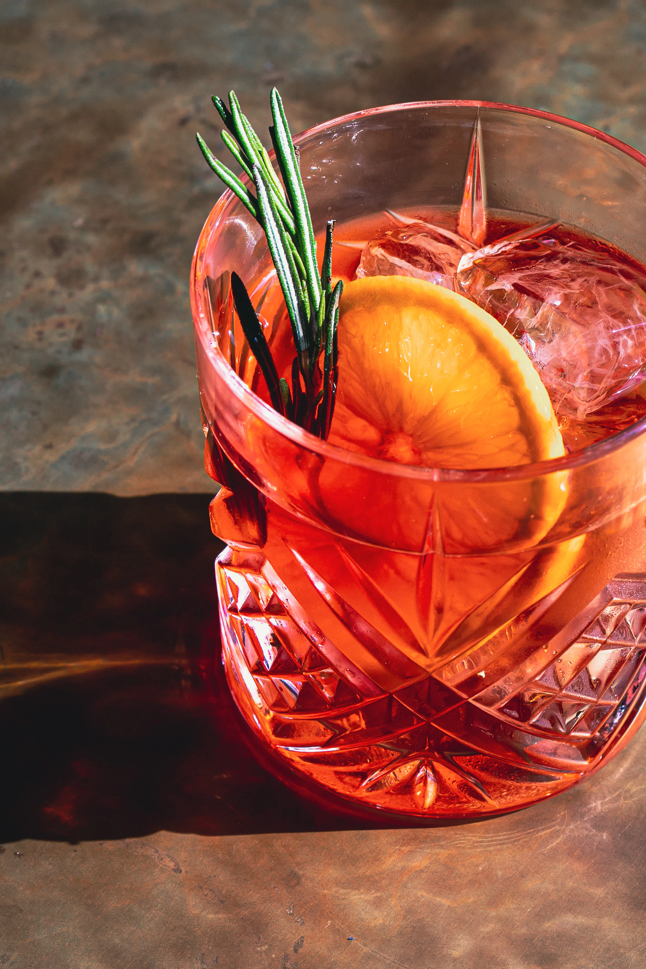 A red drink garnished with rosemary and an orange slice.