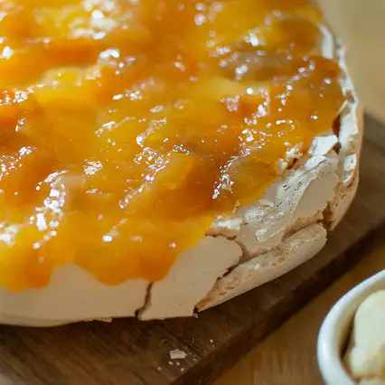 A layer of Peach Conserve is spread over a meringue base of a pavlova.