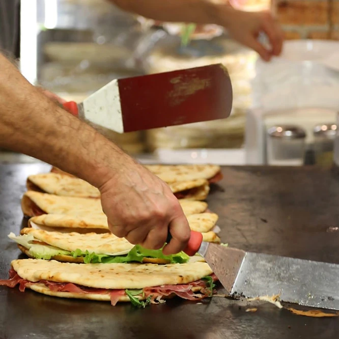 Piadina filled with rocket, tomato and prosciutto are being warmed on a grill.