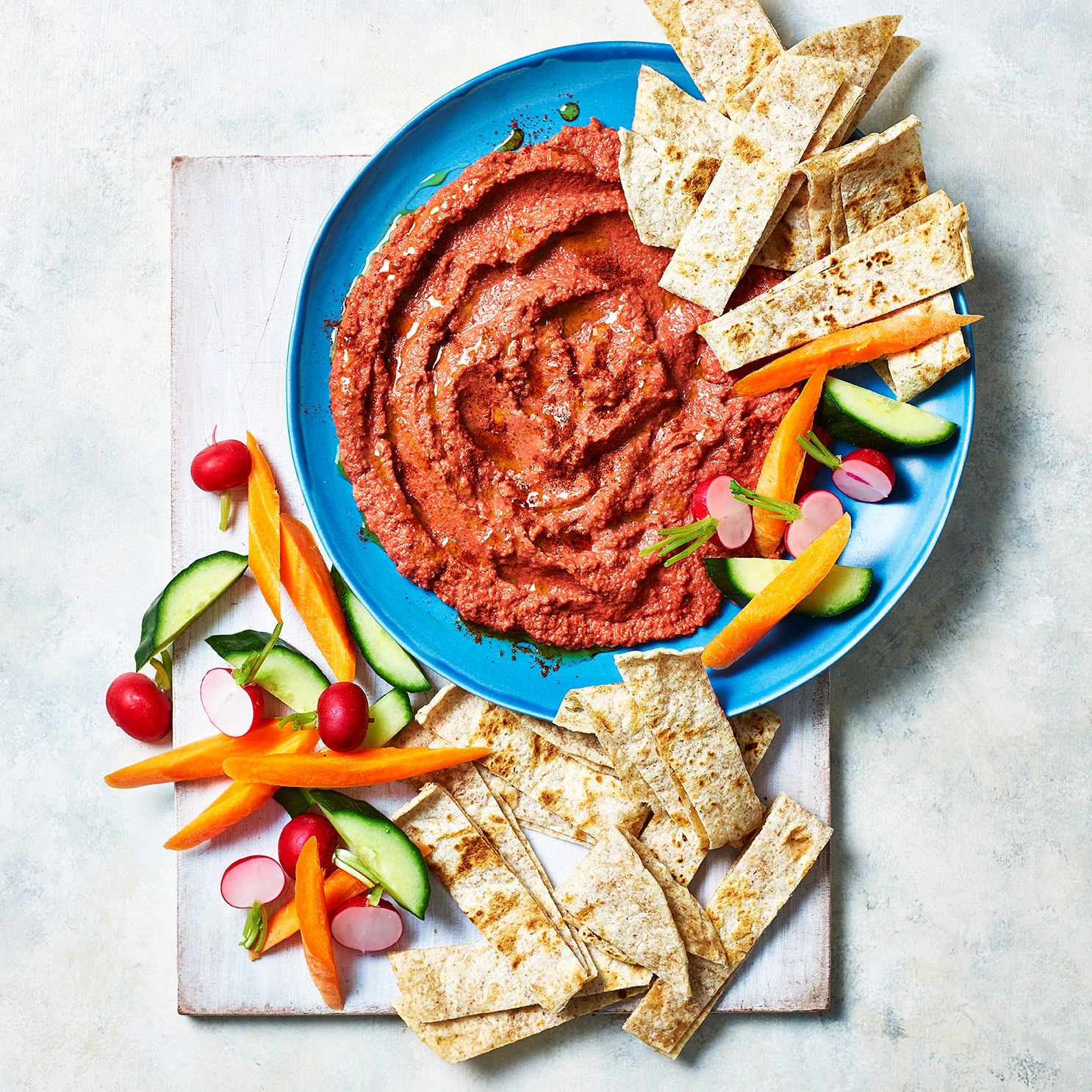 A bowl of beetroot hummus is pictured from above. Scattered around the edge of the bowl are slices of Organic Wholeblend Piadina and vegetable crudités.
