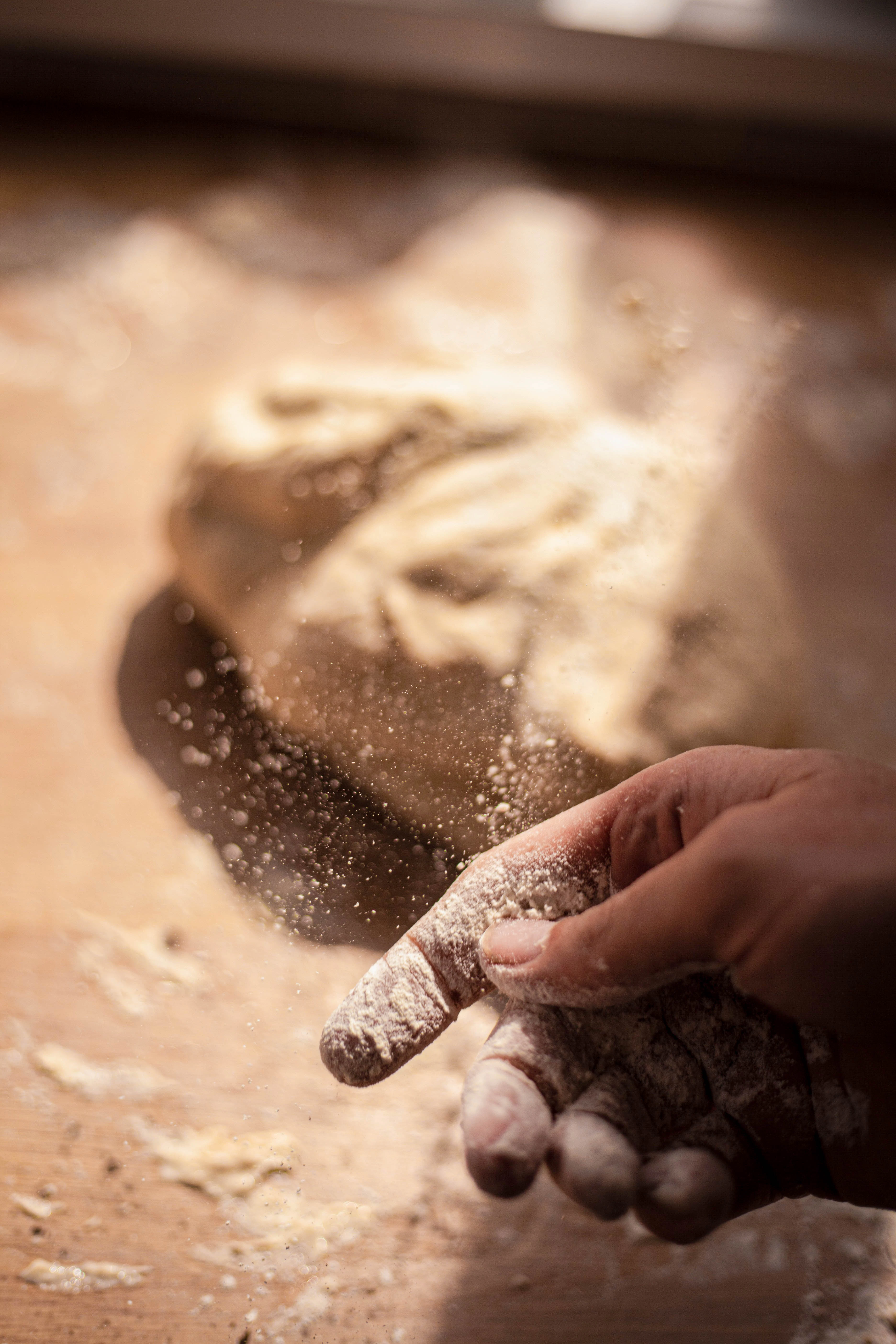 A hand covered in flour is next to a loaf of dough.