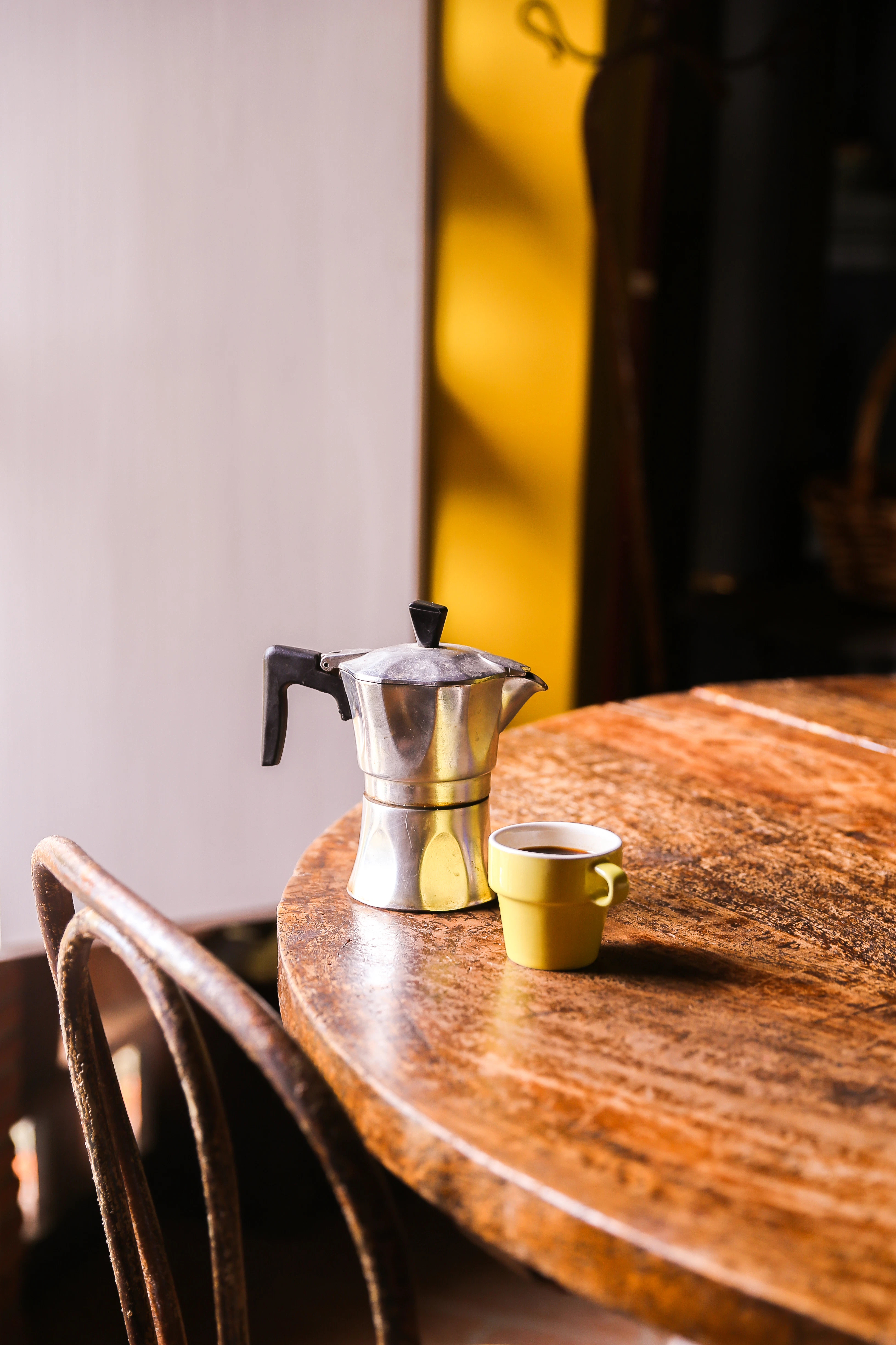 A moka pot next to an espresso cup on a table.