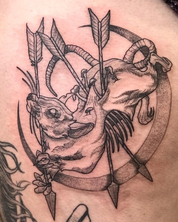 Tattoo of a decomposing rat pierced by arrows in a crescent moon frame.