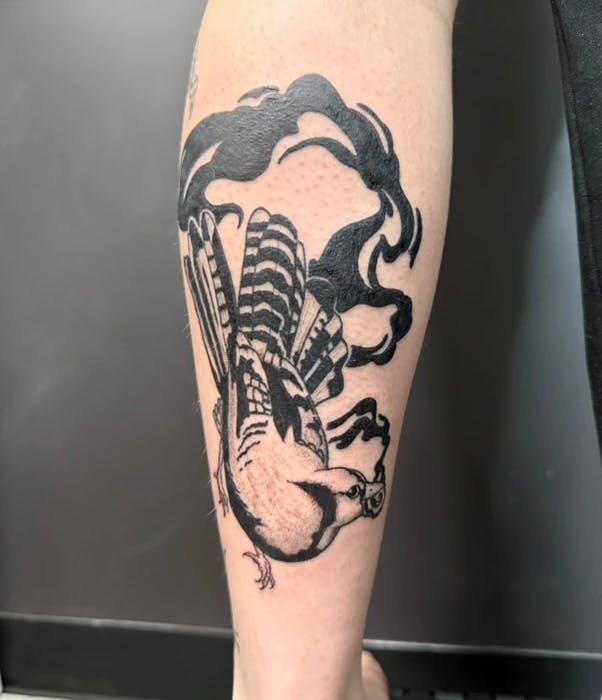 Tattoo of bird holding a round object in its mouth.