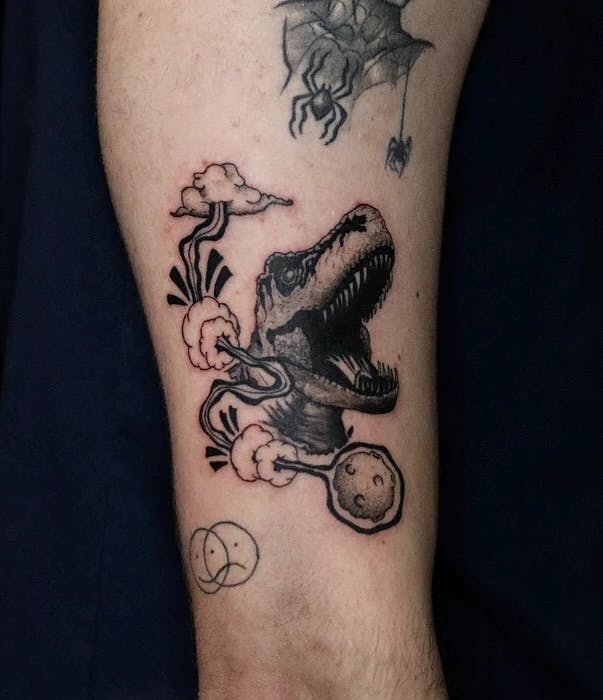 Tattoo of a t-rex head and comet.