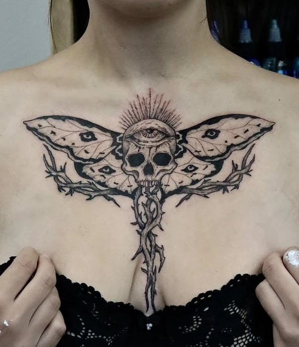 Tattoo of a radiating skull with moth wings and thorns.
