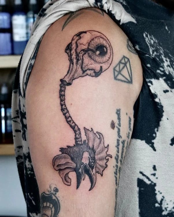 Tattoo of a rooster head with its spinal cord attached to its foot that's holding an eyeball.