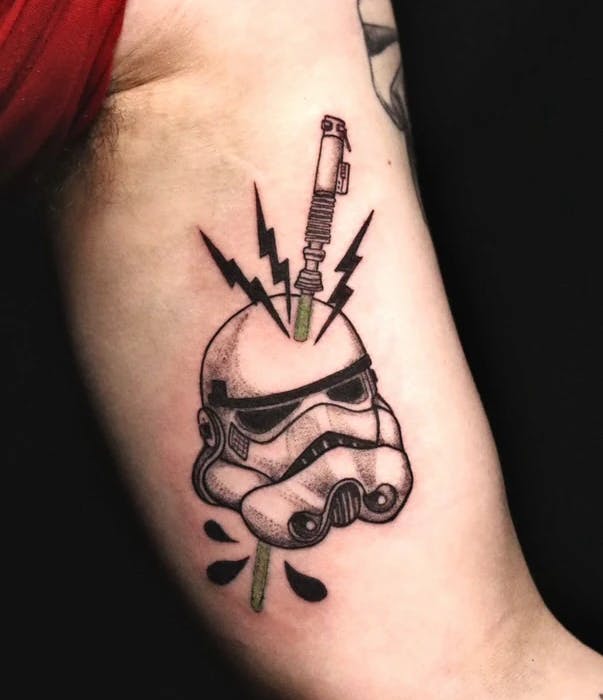 Tattoo of a stormtrooper with a lightsaber piercing through their helmet.