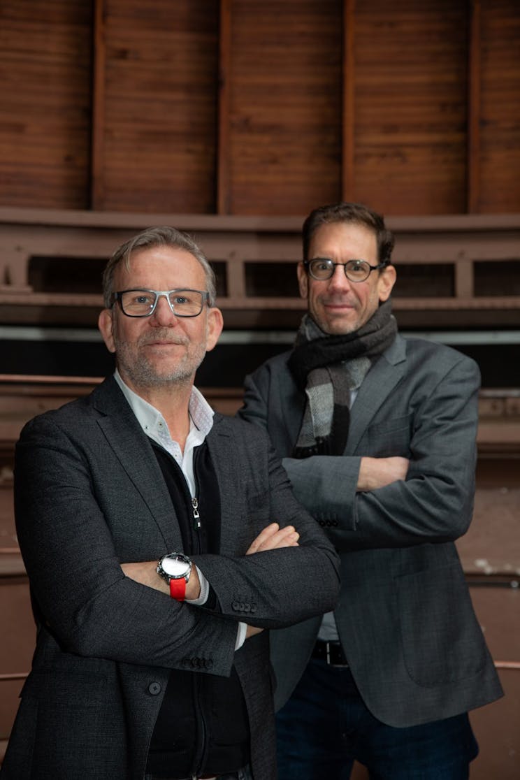 Two men standing with their arms crossed with one wearing a watch with connected fitness monitoring solutions.