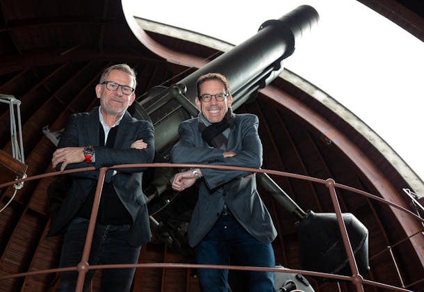 Two men standing in front of a telescope