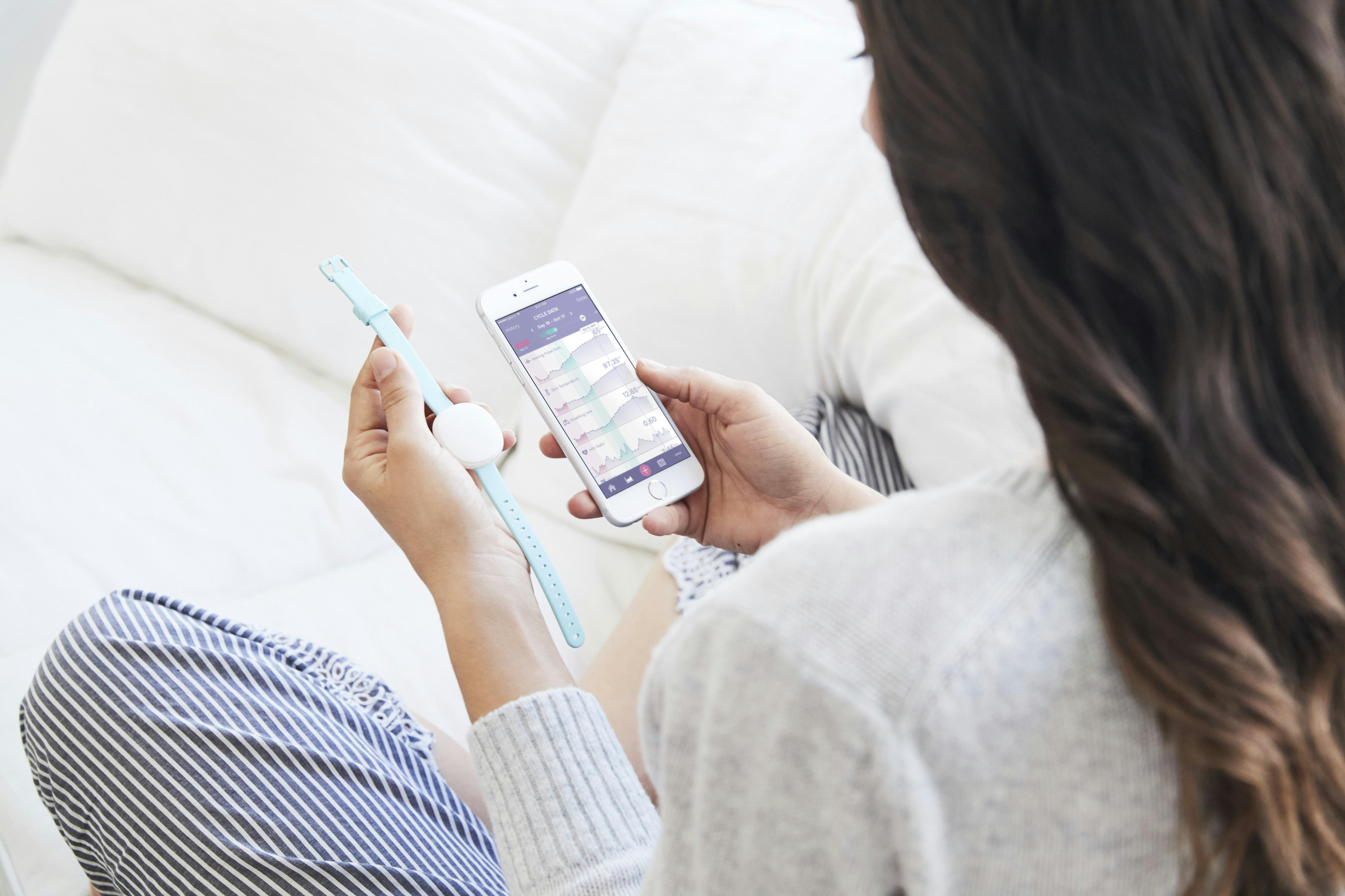 Femme tenant un smarphone et un bracelet de fertilité AVA