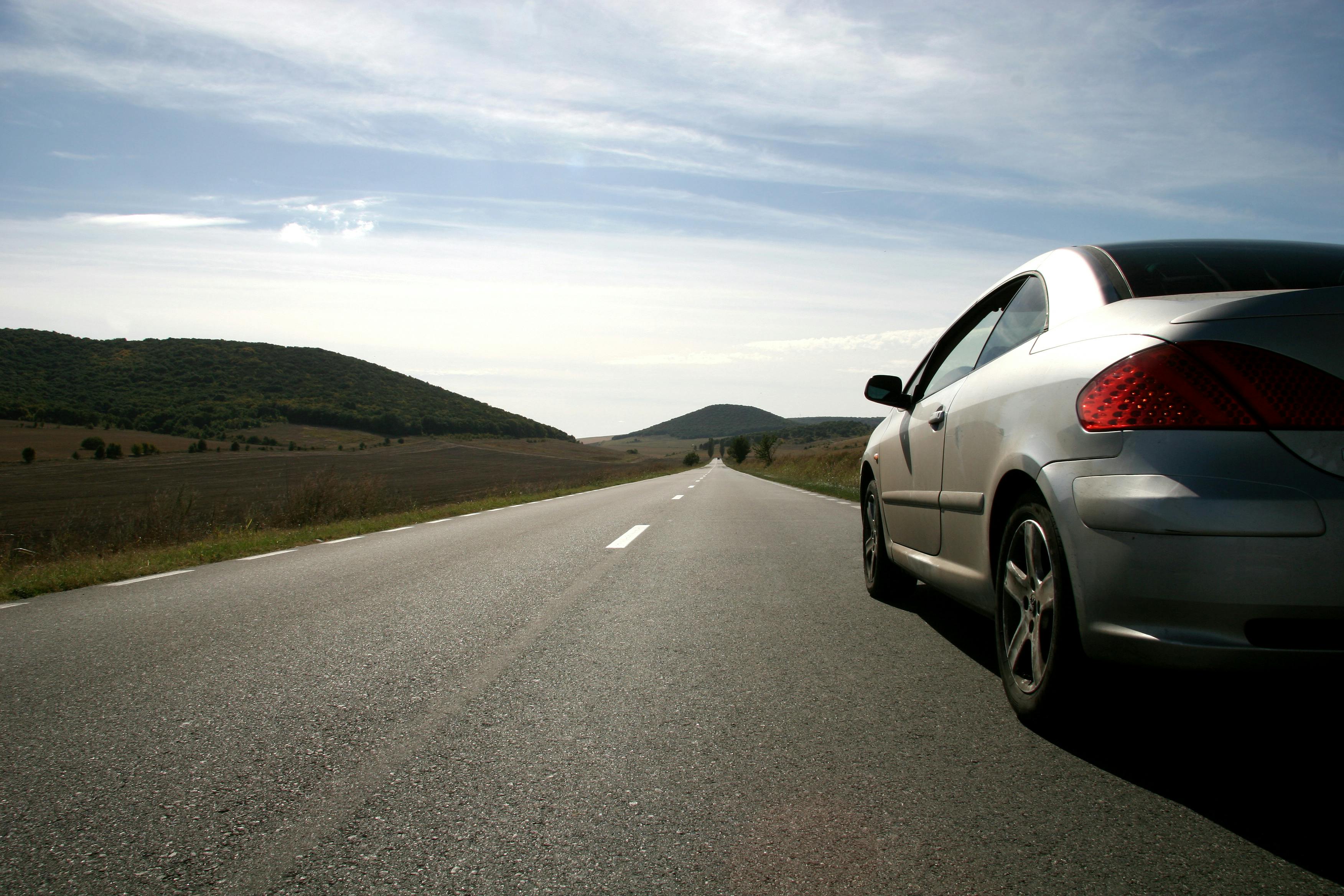 Grey car driving on a straight road, green landscape