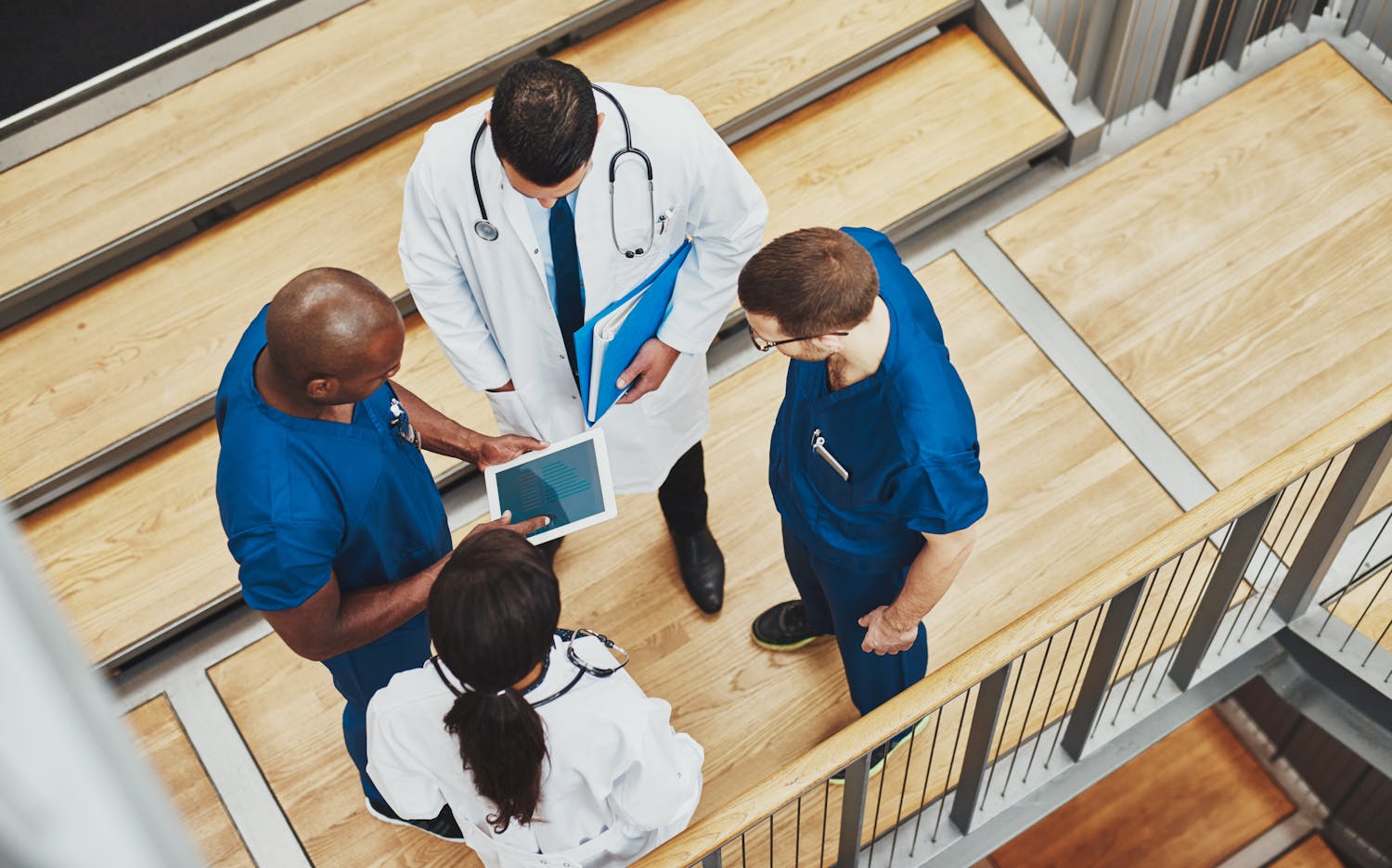 4 people standing in a small group around a tablet. 1 men and 1 women wear a medical coat.