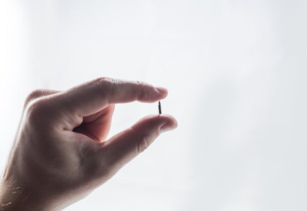 Hand holding an implantable biosensor, the size of a match, approx. 1 cm long