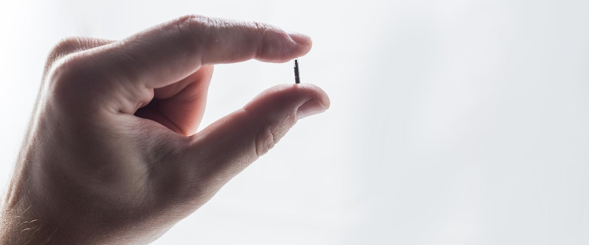 Hand holding the implantable biosensor CERES between finger and thumb: the size is similar to a 1cm tall match