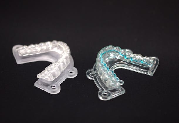 Deux prototypes d'Active Aligner équipés de diffuseurs antibactériens. Le prototype de droite contient un liquide bleu mettant en évidence l'innovation : un système de microcanaux imprimé en 3D. Celui de gauche représente le prototype d'aligneur transparent dans son apparence finale.