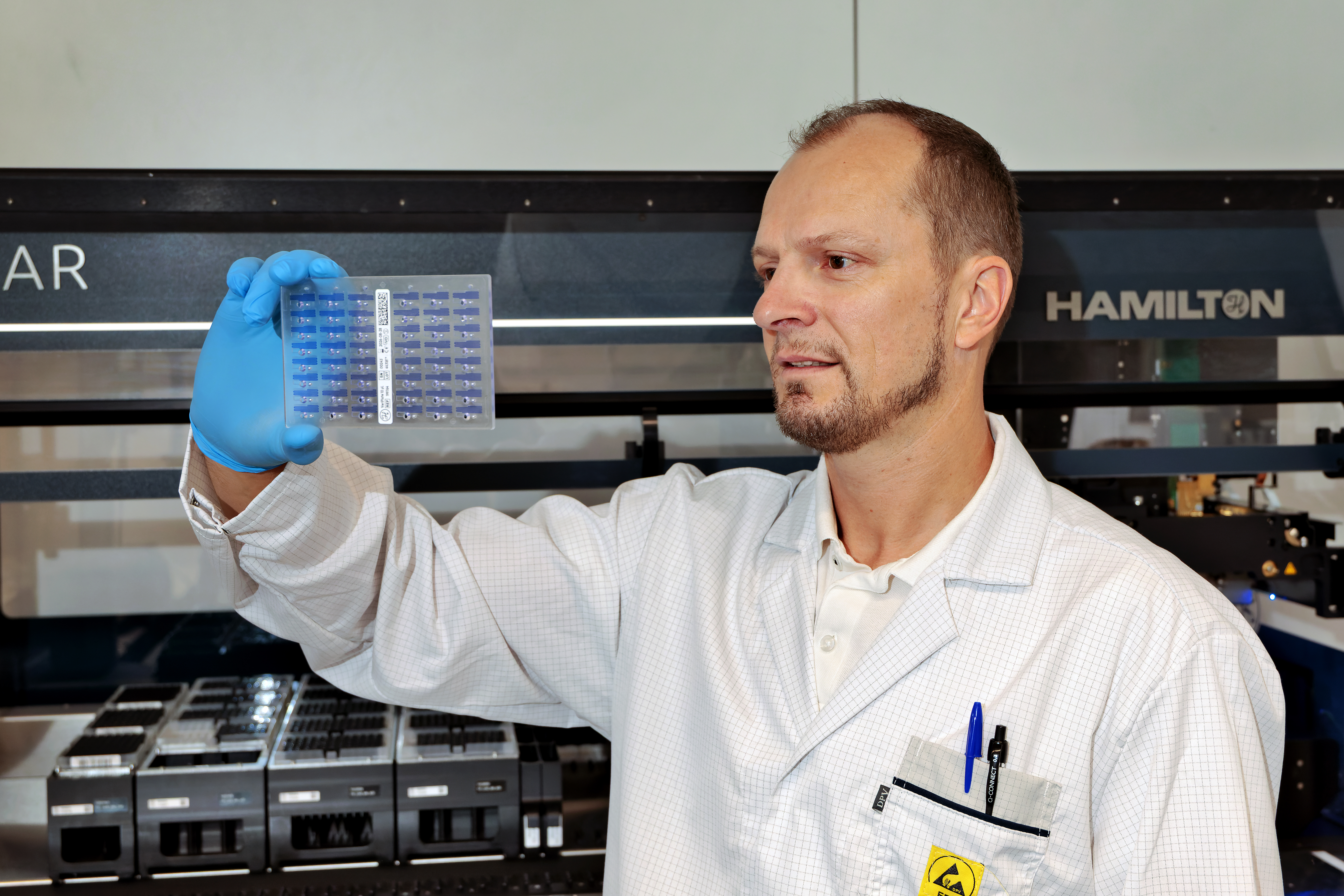 Man in a lab holding an SBS plate containing 48 capillary slots.