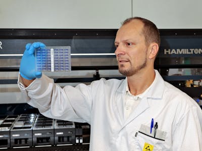Man in a lab holding an SBS plate containing 48 capillary slots.