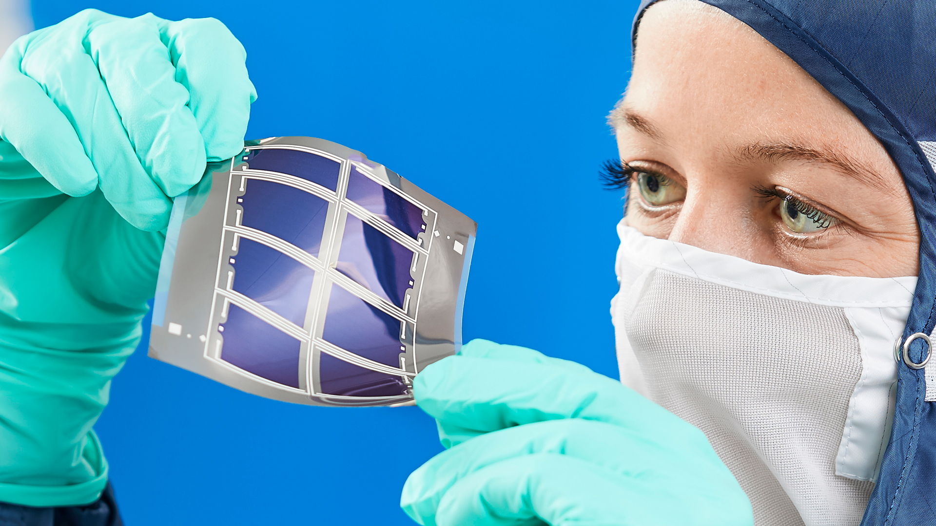Engineer in cleanroom holding a thin, flexible, and adhesive photovoltaic (PV) foil