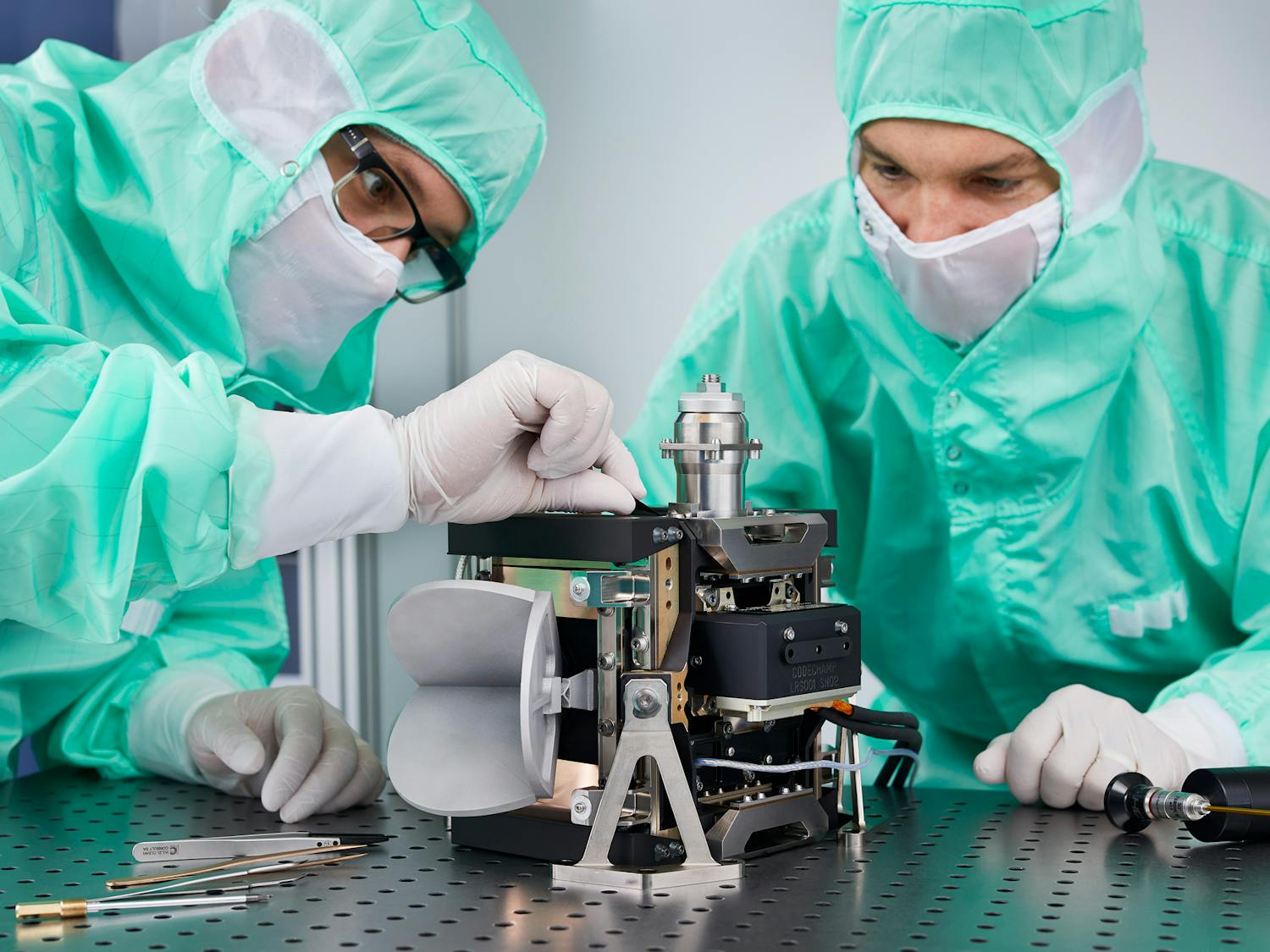 Two engineers assembling a high-precision optical device, the Corner Cube Mechanism, on a vibration-isolated table