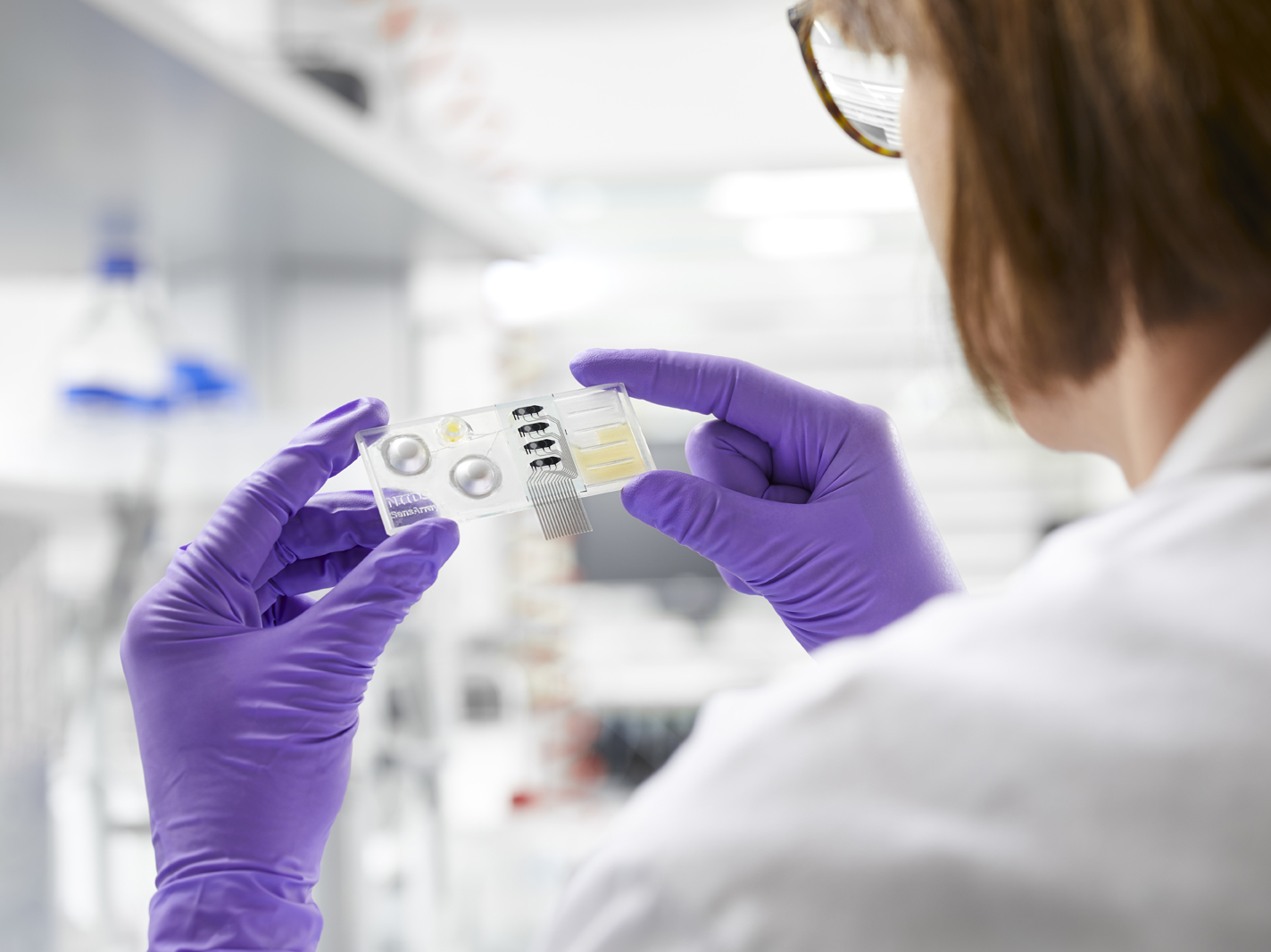 Picture of a woman in lab coat and gloves holding a device