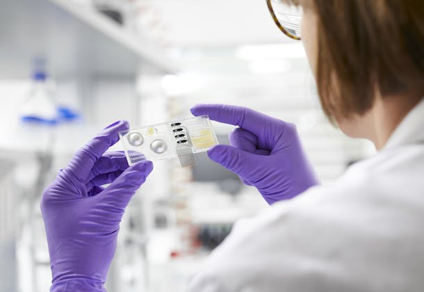 Picture of a woman in lab coat and gloves holding a device