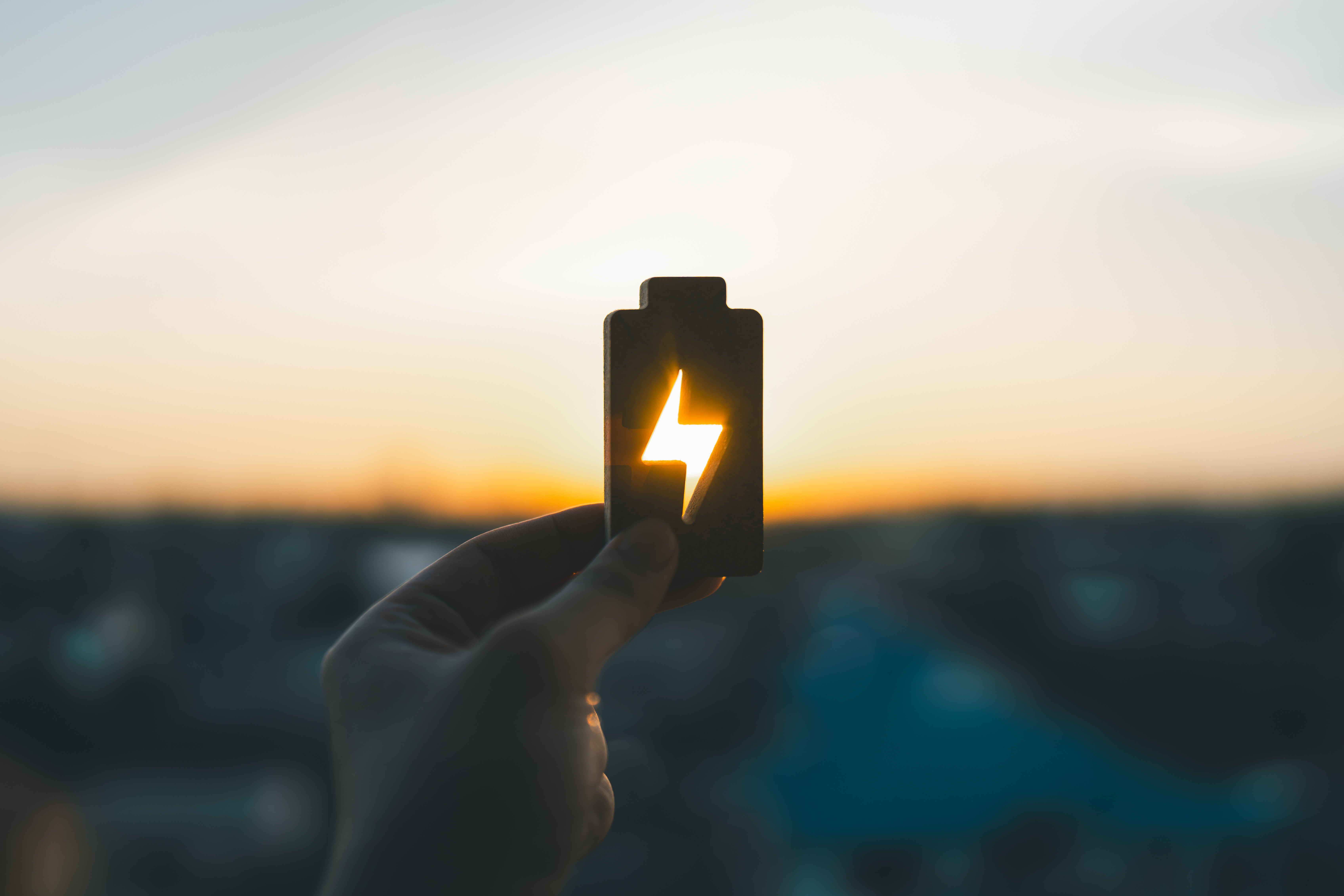Hand holding battery icon with lightning symbol representing renewable energy and power storage at sunset