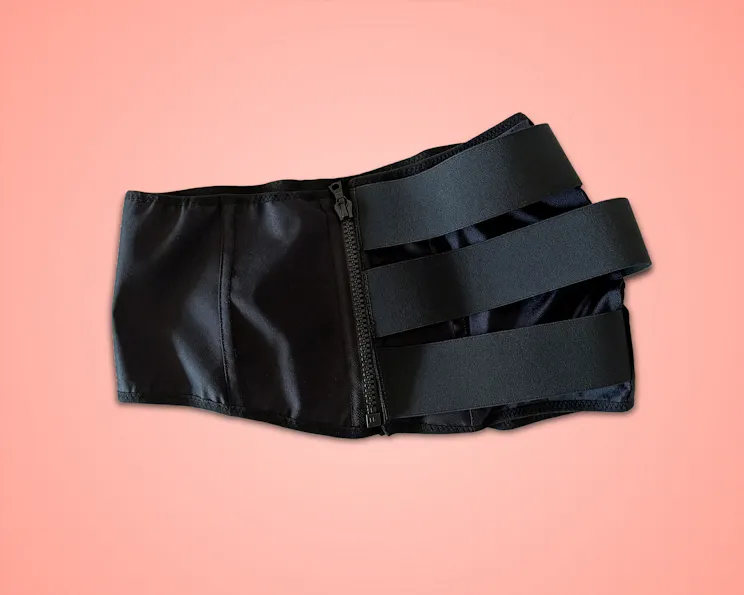 Flat lay of the black VidaSense band with a zipper and elastic straps, shown against a pink background.