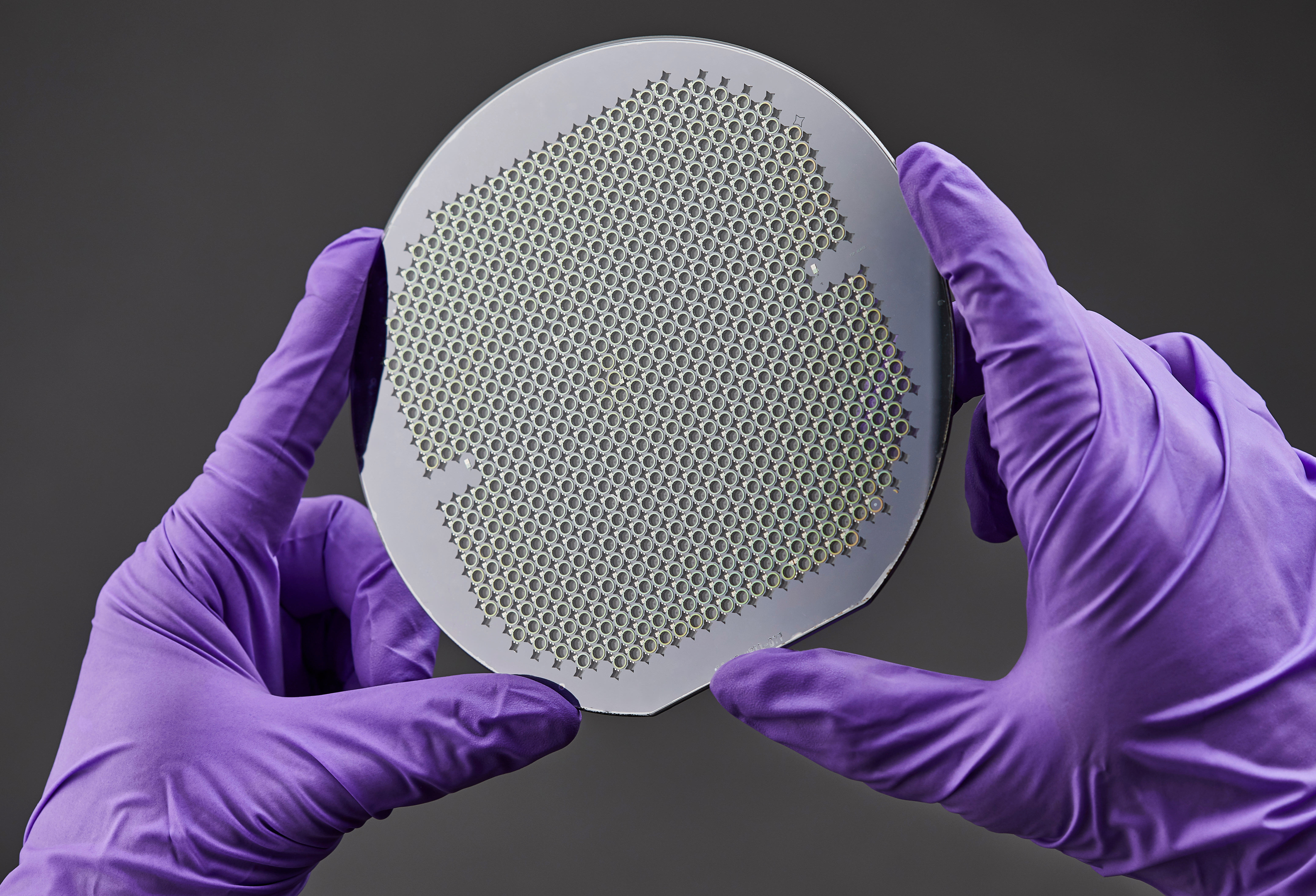 Wafer of MEMS atomic vapor cells held in gloved hands.