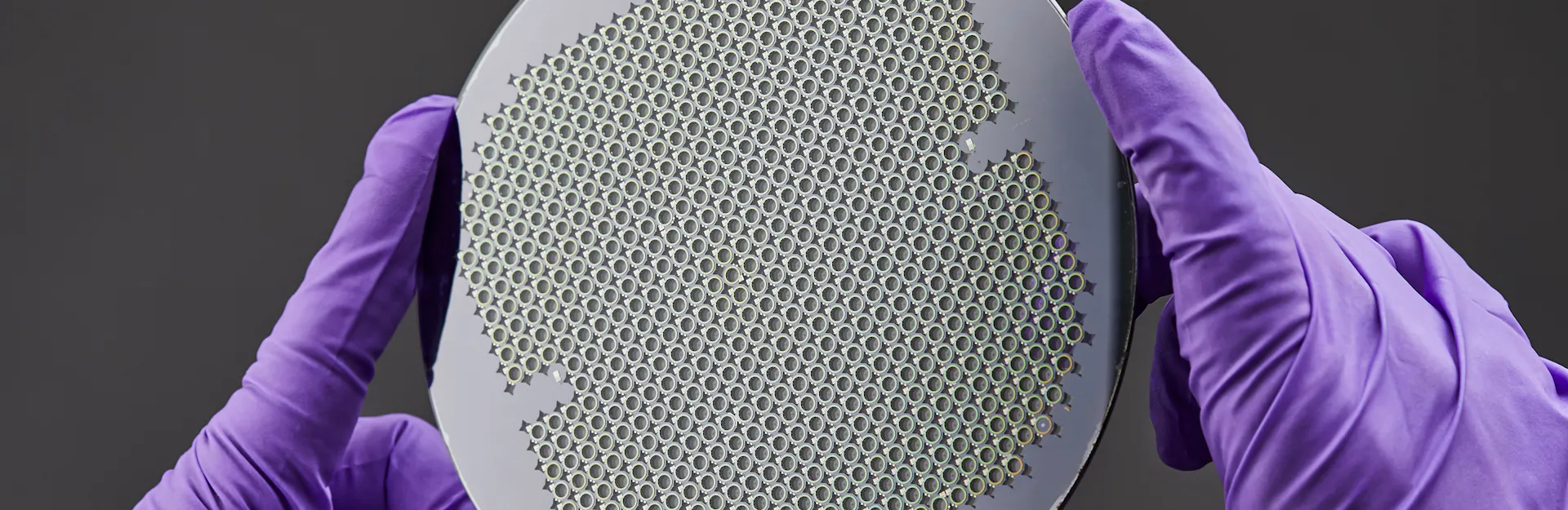 Wafer of MEMS atomic vapor cells held in gloved hands.