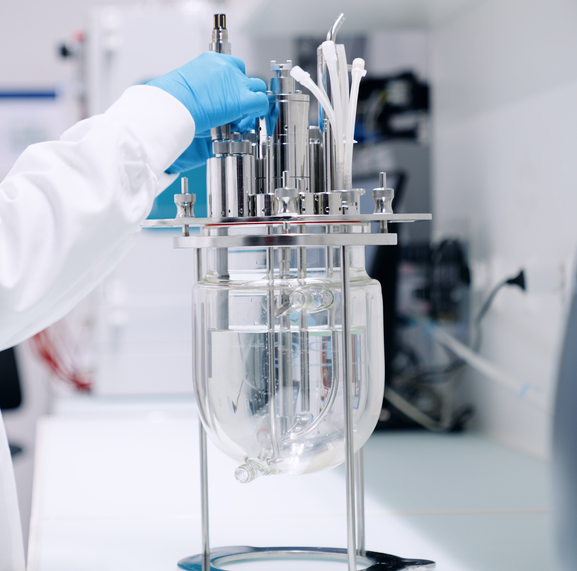 Close-up of a technician installing a Hamilton GlucoSense sensor into a glass bioreactor vessel in a laboratory setting.