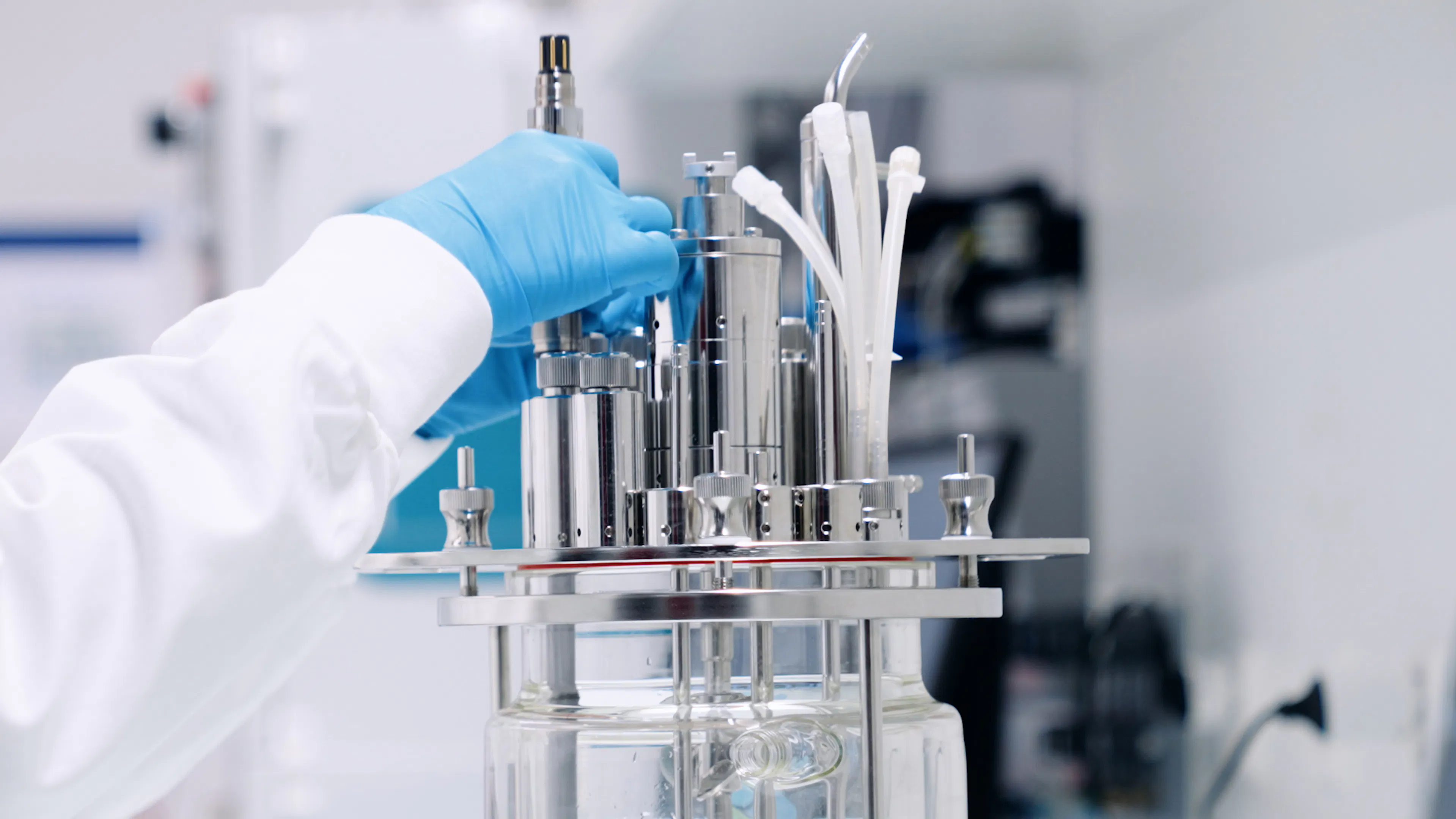 Close-up of a technician installing a Hamilton GlucoSense sensor into a glass bioreactor vessel in a laboratory setting.