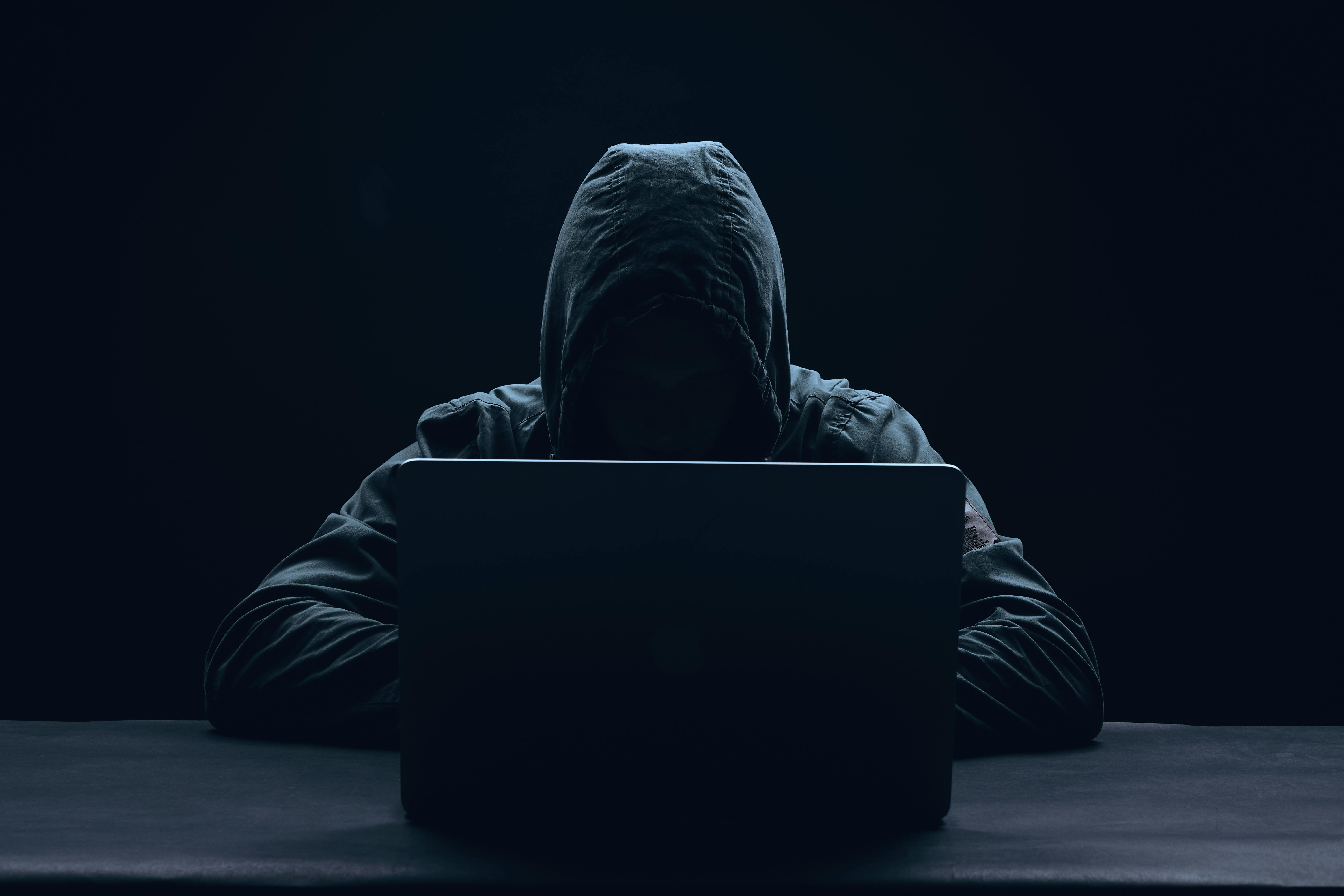 Hacker mit schwarzer Kapuze, der vor einem Computer sitzt