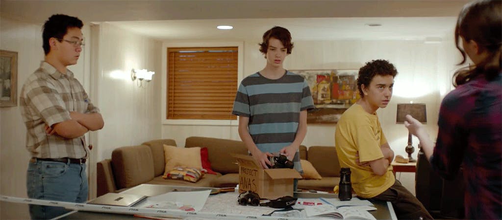Four teenagers inside a living room with papers covering a table