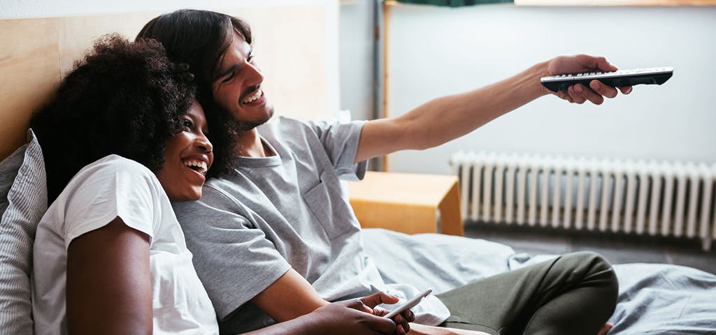 man and woman smiling while watching something offscreen - man is holding a remote control