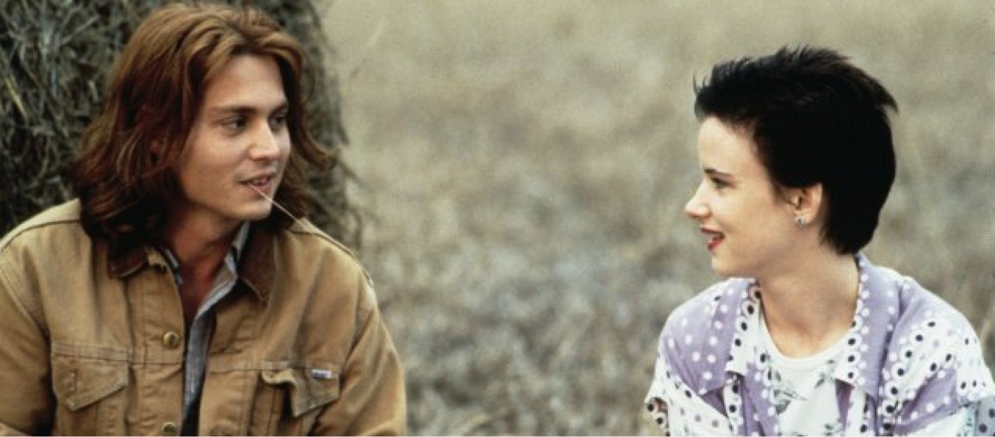 man sitting against haybale, smiling at woman sitting close by