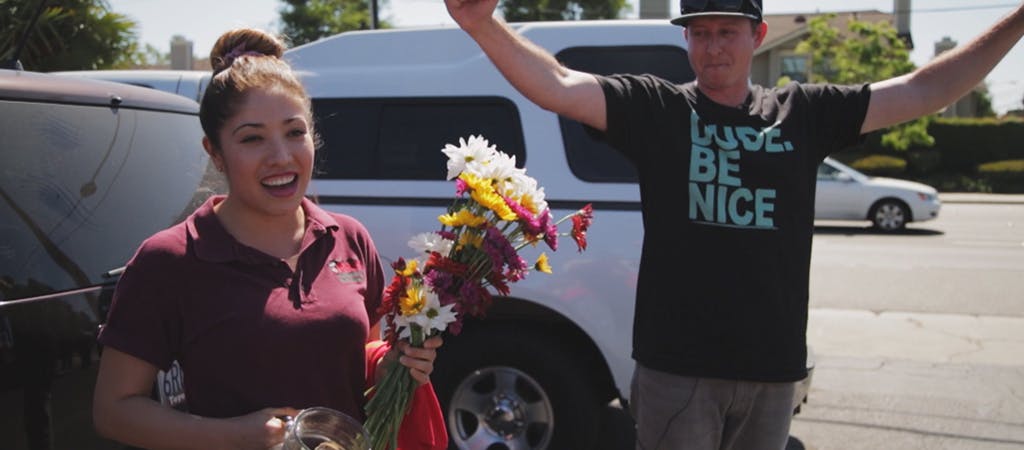 Smiling woman holding flower bouquet, and a smiling man with arms raised